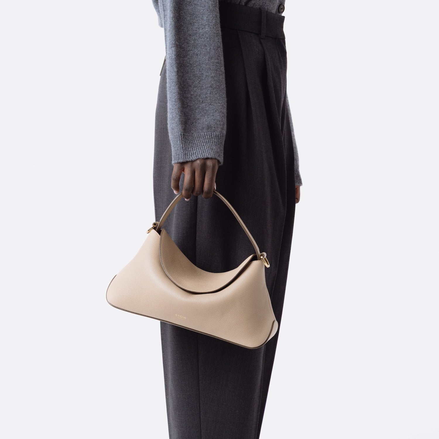 Model holding STOW London's East West in Camel pebbled leather at her side on a white background