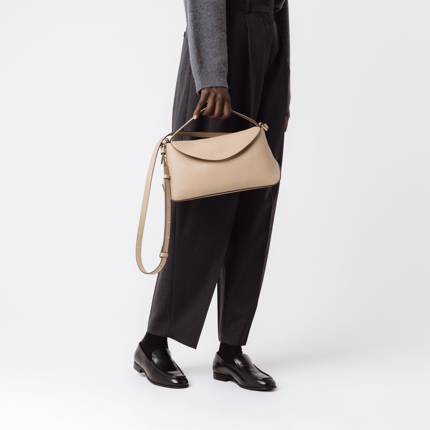 STOW London's East West in Camel leather held by the top handle at model's side, on a white background