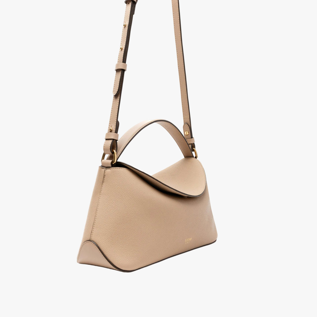 Off-axis view of STOW London's East West in Camel pebbled leather featuring the crossbody strap attached by gold-coated stainless steel hardware on a light grey background