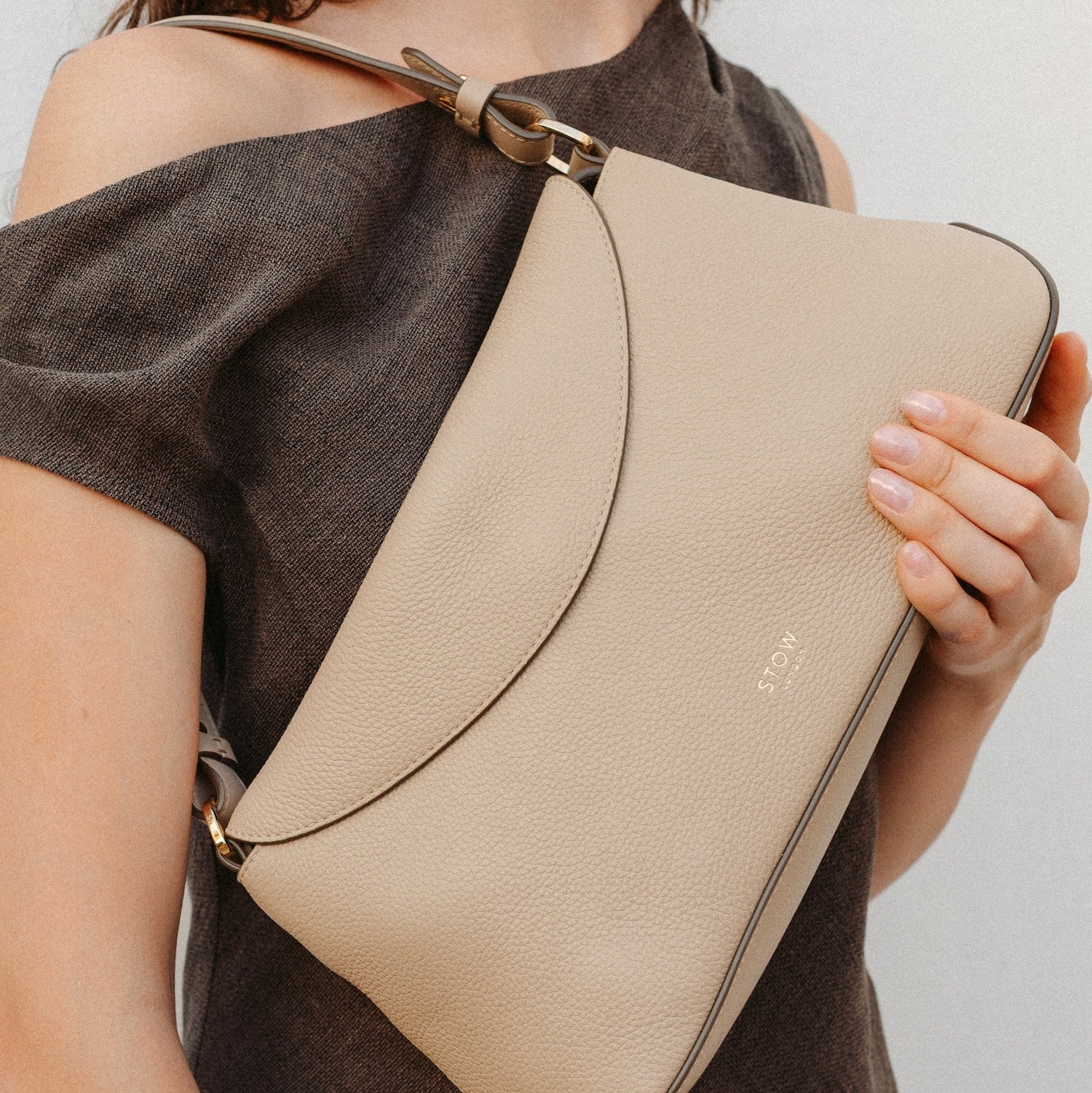 Model holding STOW London's East West in Camel leather featuring the detachable shoulder strap with gold hardware and details