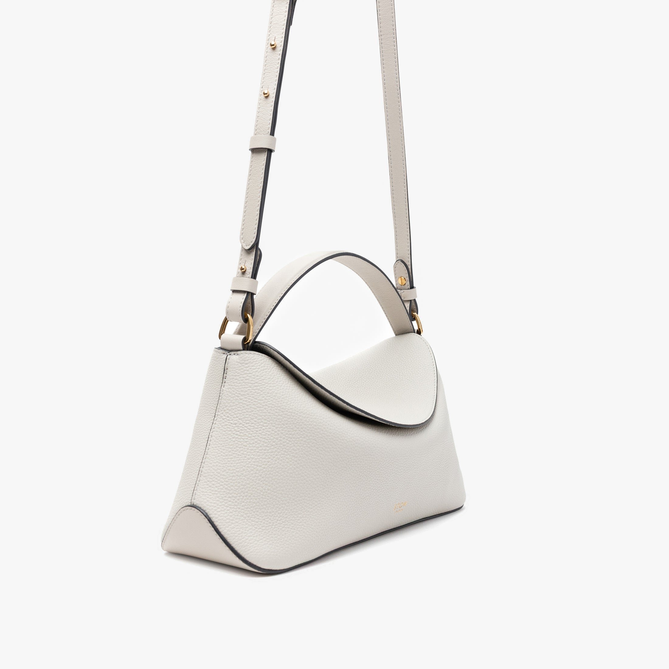 Off-axis view of STOW London's East West in Cloud Grey pebbled leather and detachable crossbody strap featuring gold-coated stainless steel hardware on a light grey background