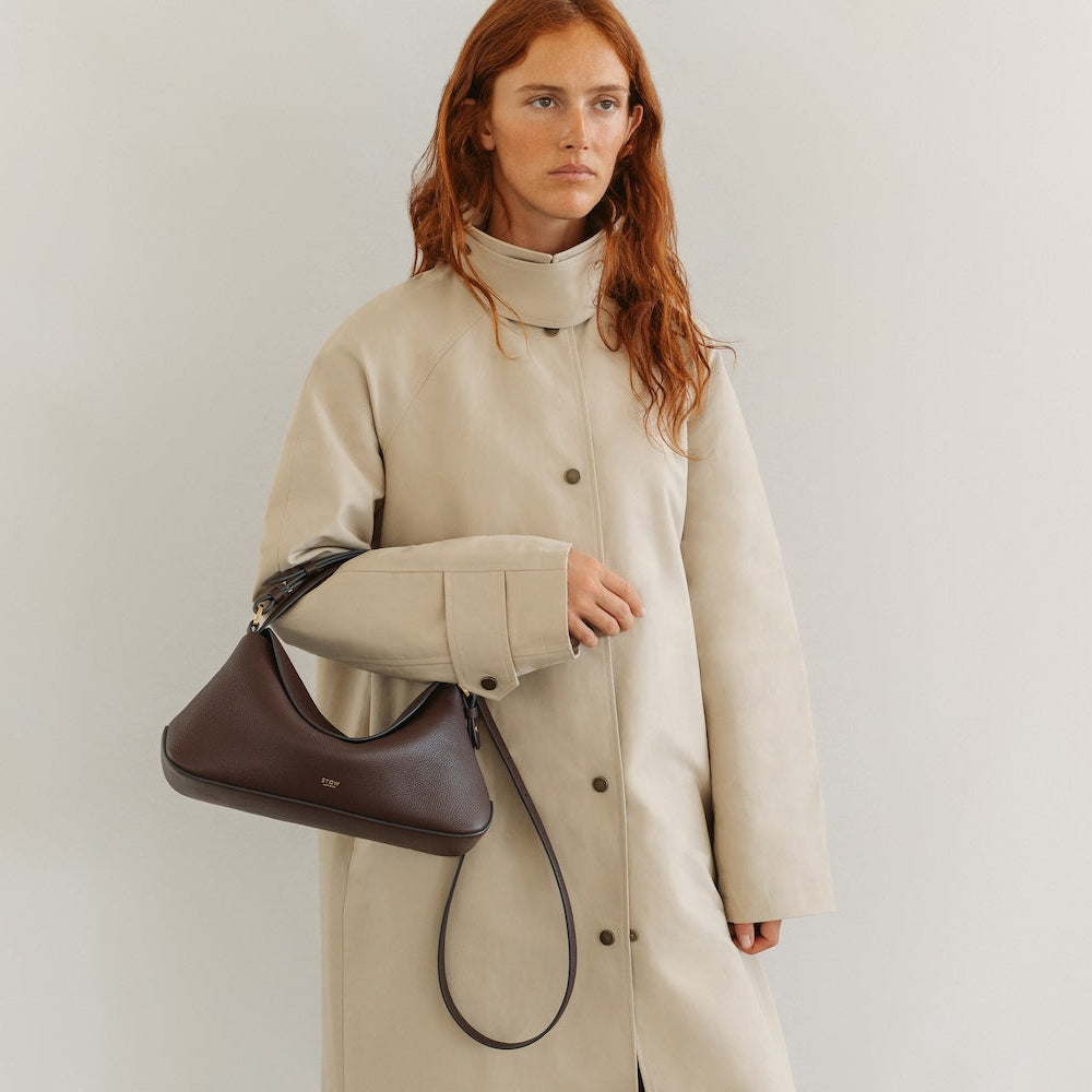 Model in a beige coat styling STOW London's East West in Espresso pebbled leather featuring gold-coated stainless steel hardware
