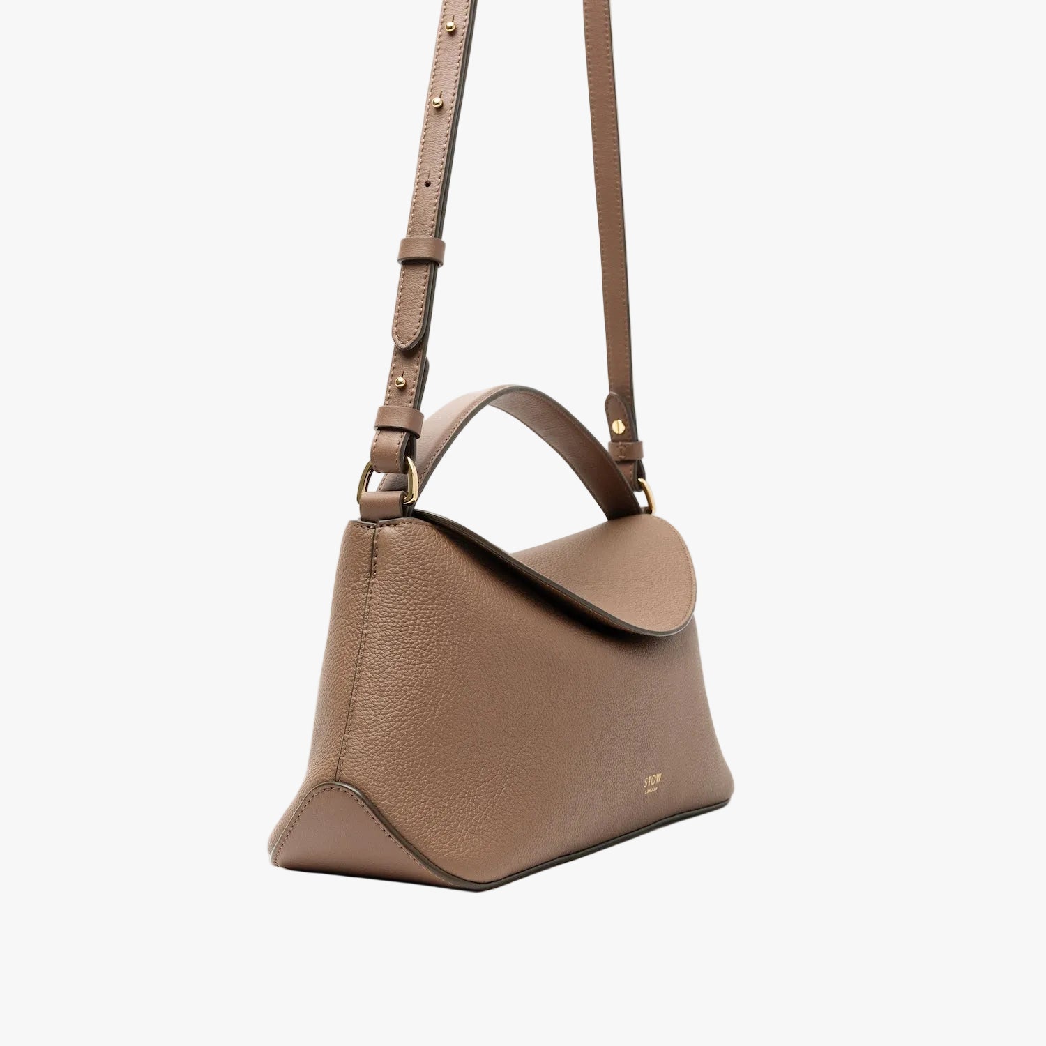 Off-axis view of STOW London's East West bag in Mocha pebbled leather featuring the crossbody strap attached with gold-coated stainless steel hardware on a light grey background