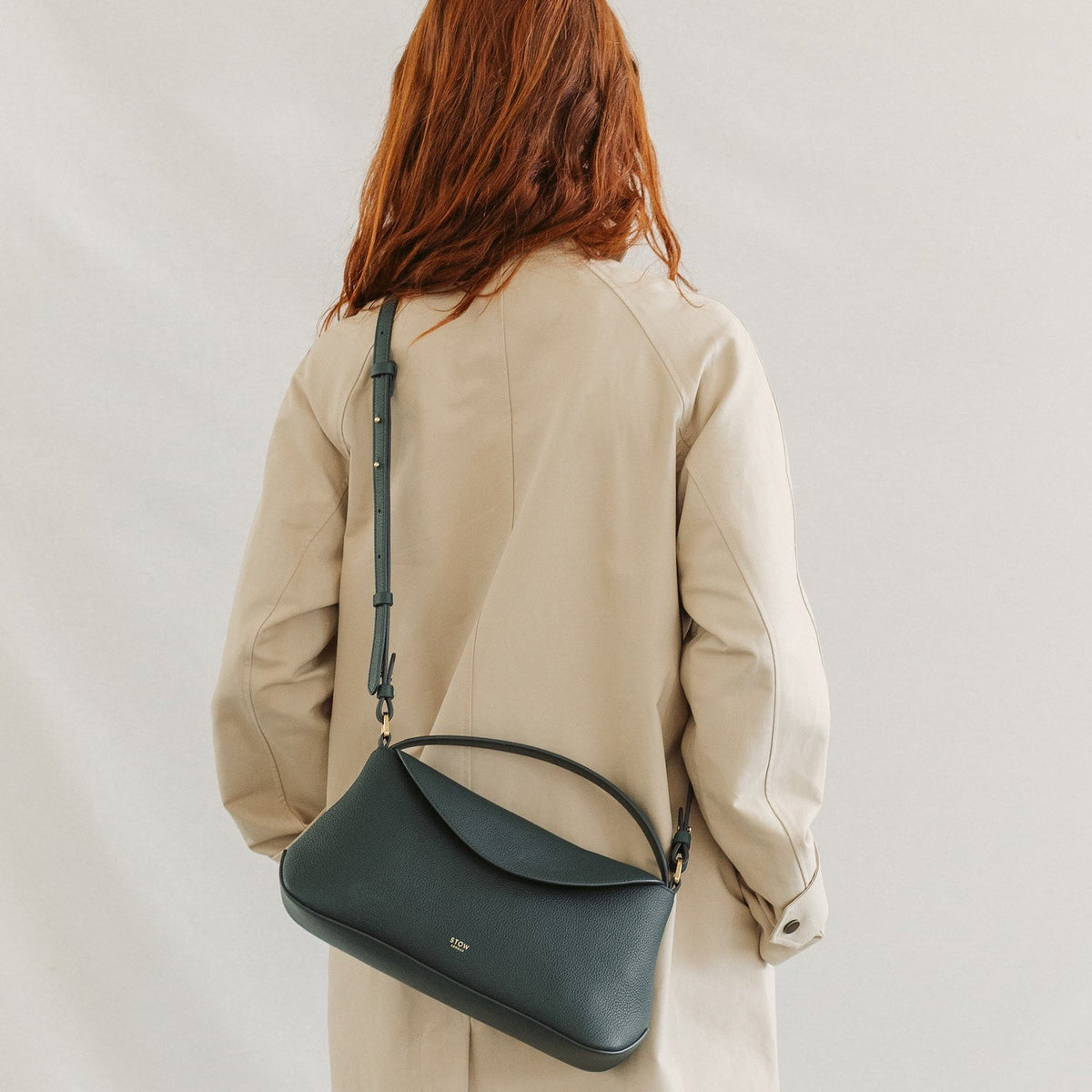 Model in a beige coat wearing STOW London's East West in New Forest pebbled leather crossbody featuring gold-coated stainless steel hardware
