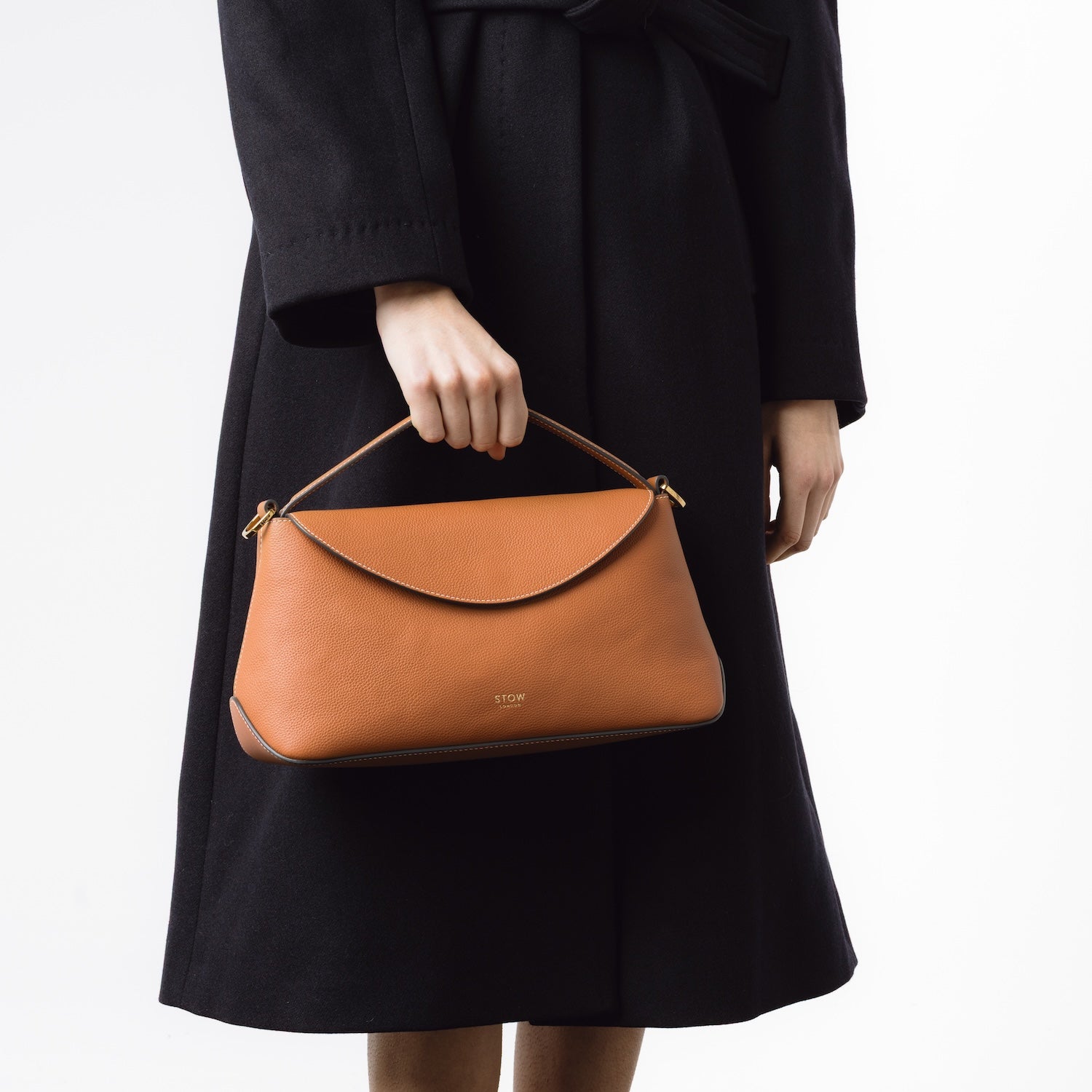 STOW London's East West bag in Earth Tan featuring gold-coated stainless steel hardware held by handle by model on a white background