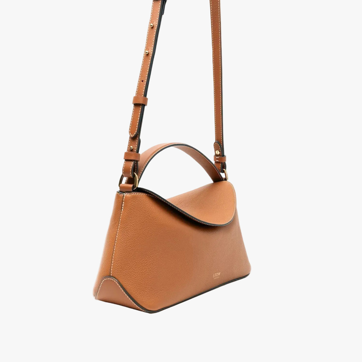 Off-axis view of STOW London's East West bag in Earth Tan pebbled leather and crossbody strap featuring gold-coated stainless steel hardware on a light grey background