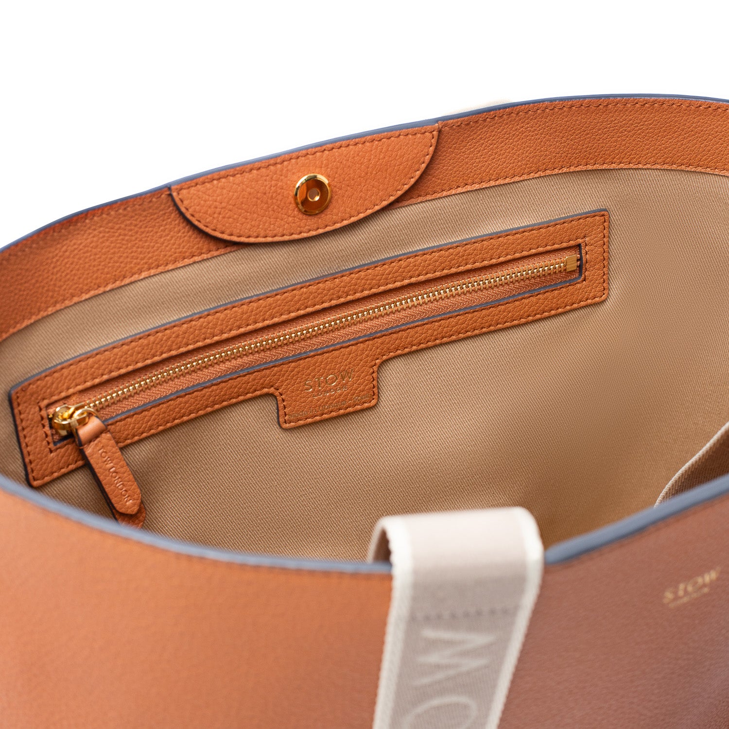 Close up of interior of STOW London's Nastro Tote bag in Earth Tan pebbled leather featuring the interior zipped pocket and magnetic closure on a white background