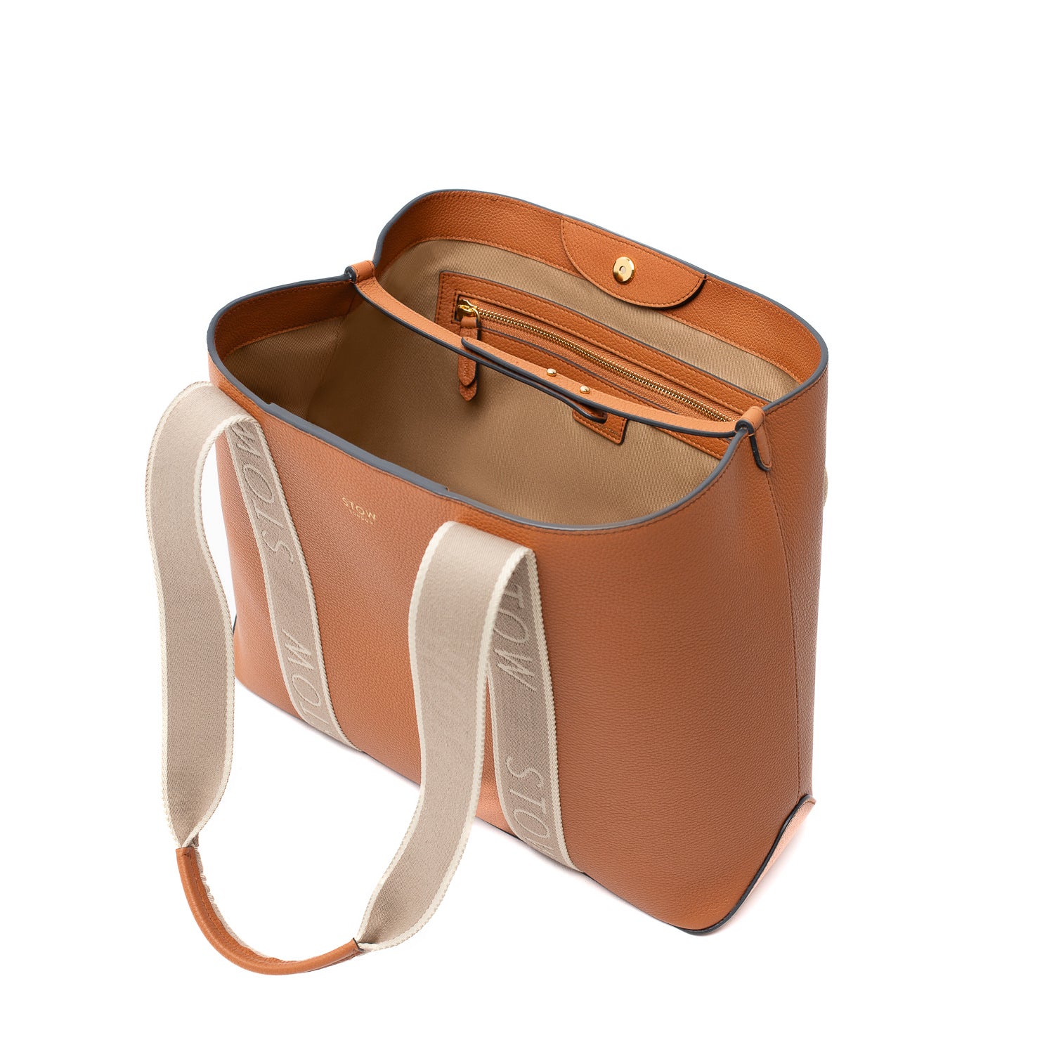 Elevated angle view of STOW London's Nastro Tote bag in Earth Tan with magnets open but interior leather strap done up showing the cotton interior lining and zipped pocket featuring gold hardware, on a white background.