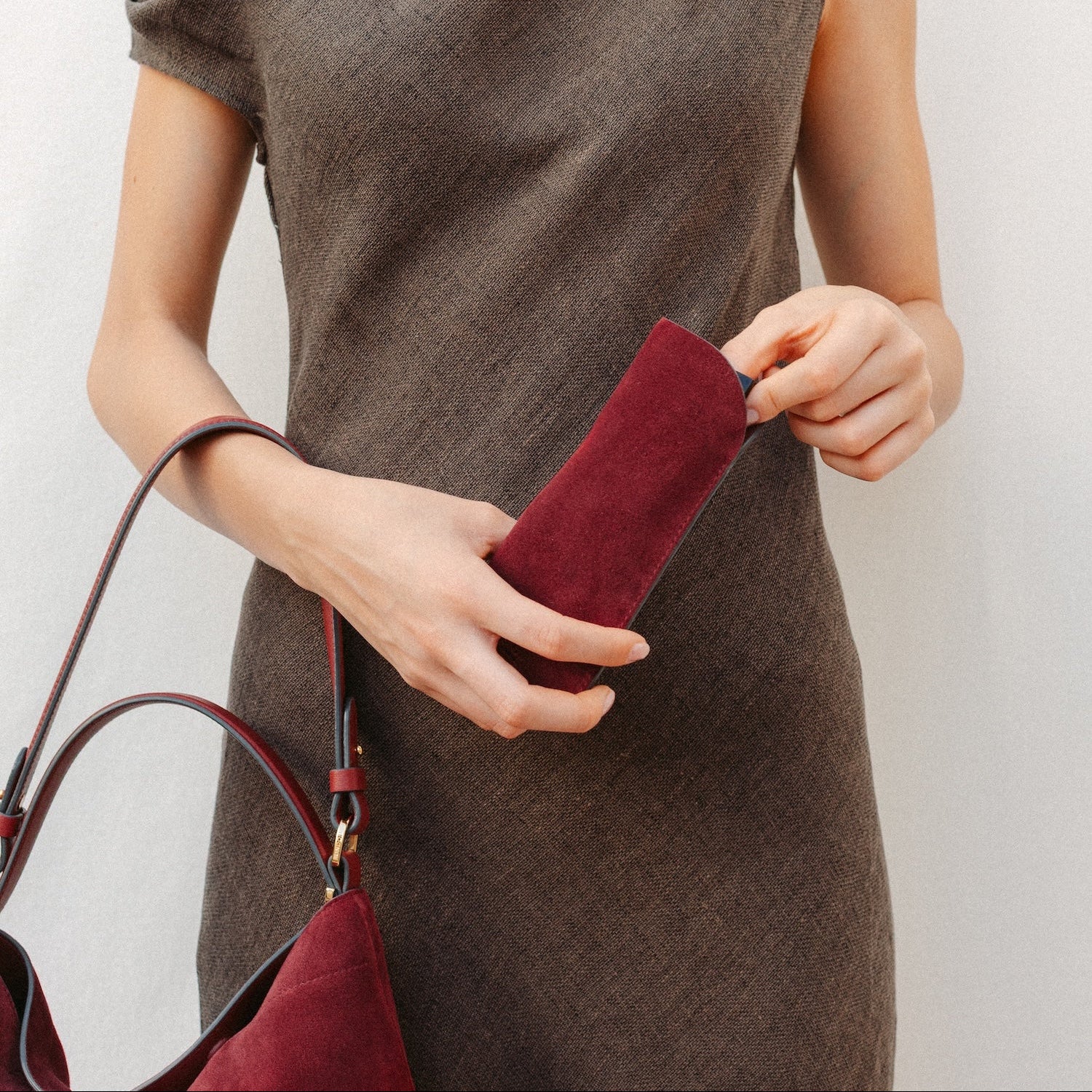 Model putting her glasses into STOW London's Glasses Case in Burgundy suede leather with the Burgundy suede Curve on her arm