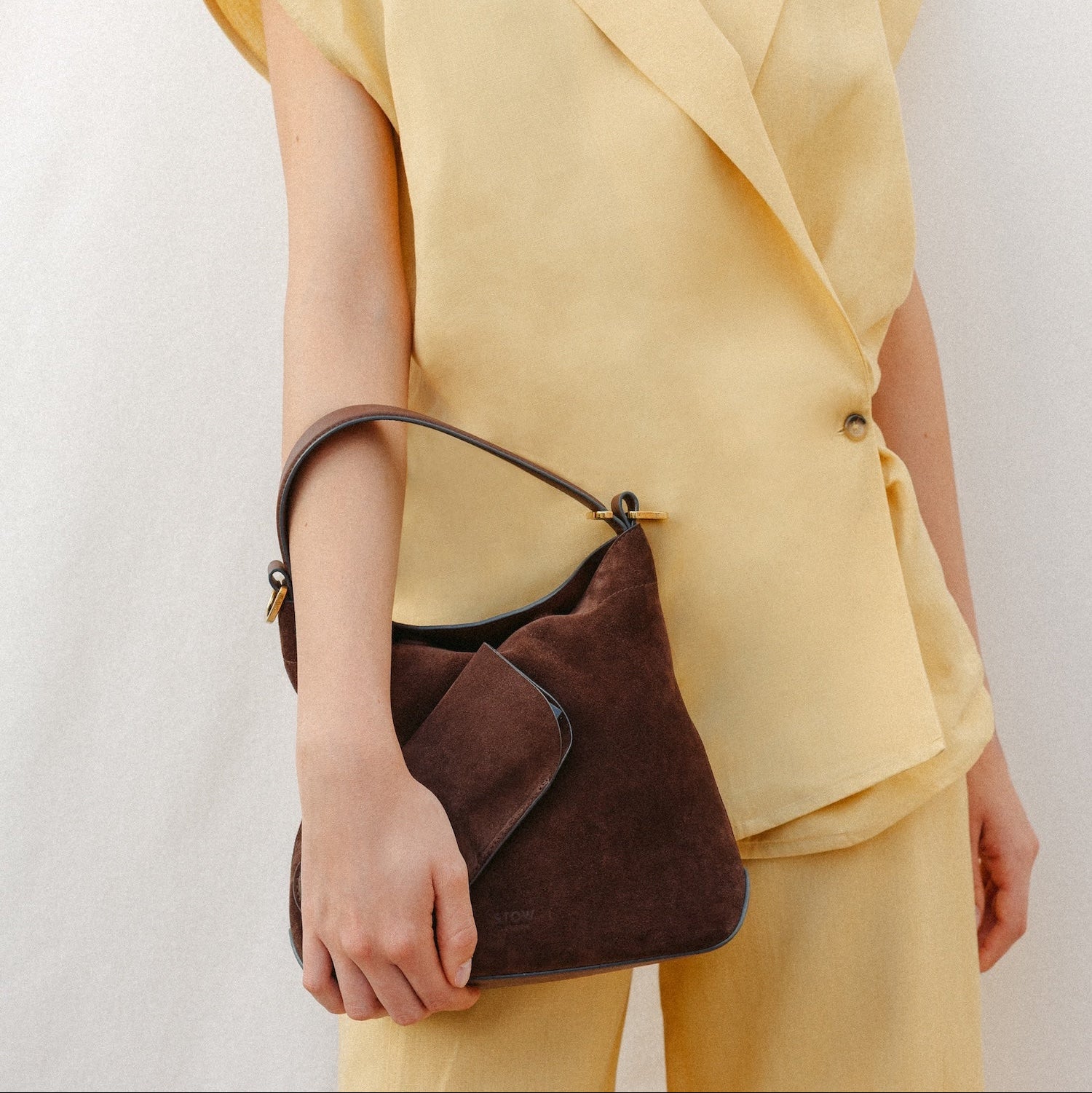 Model wearing a yellow outfit holding STOW London's Glasses Case and Midi Curve in Chocolate suede leather at her side
