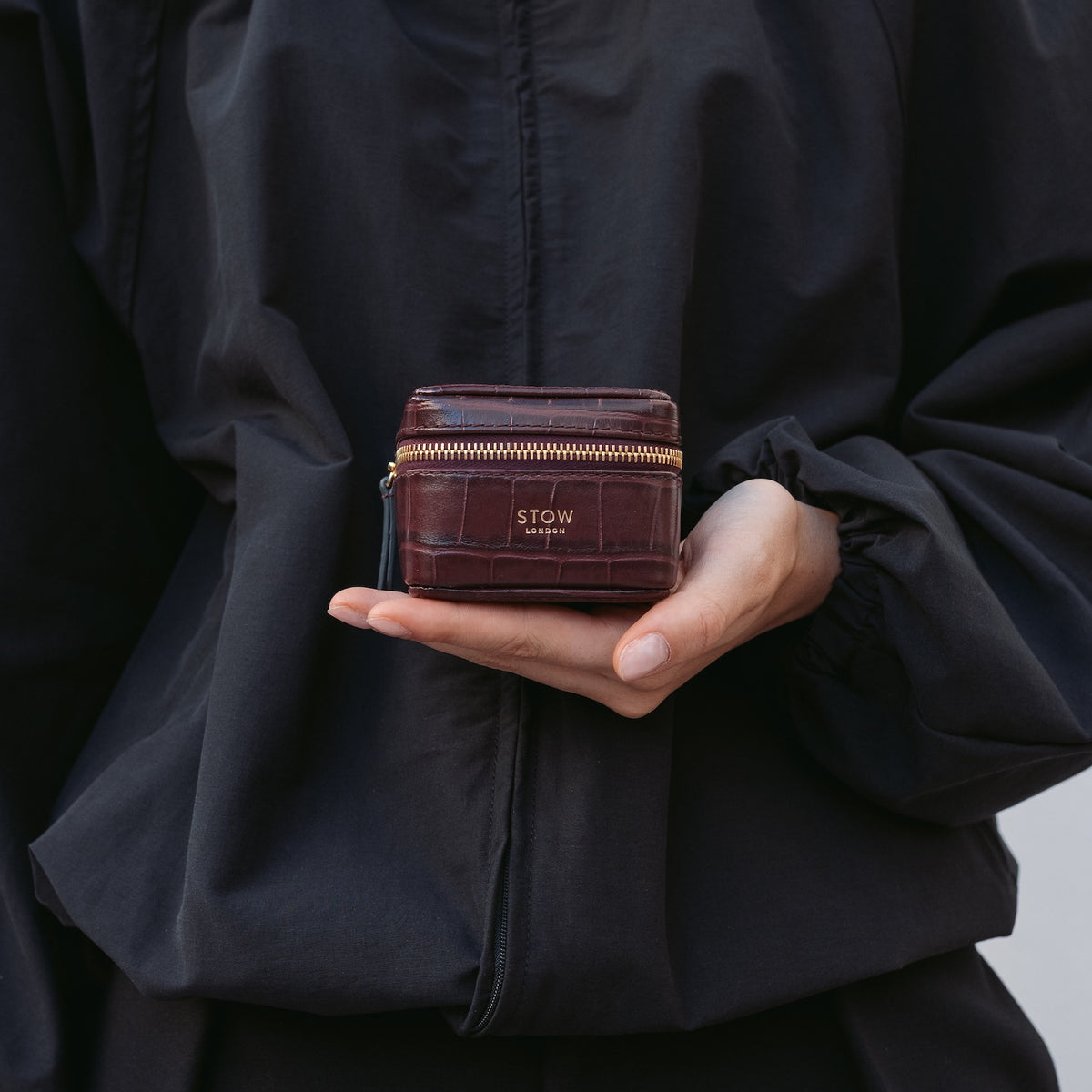 Model holding STOW London's Hester Jewellery Case in Burgundy embossed croc leather featuring a small gold embossed logo on the front