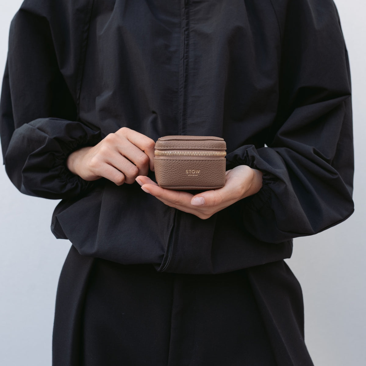 Model holding STOW London's Hester Jewellery Case in Mocha pebbled leather featuring a small gold embossed logo on the front