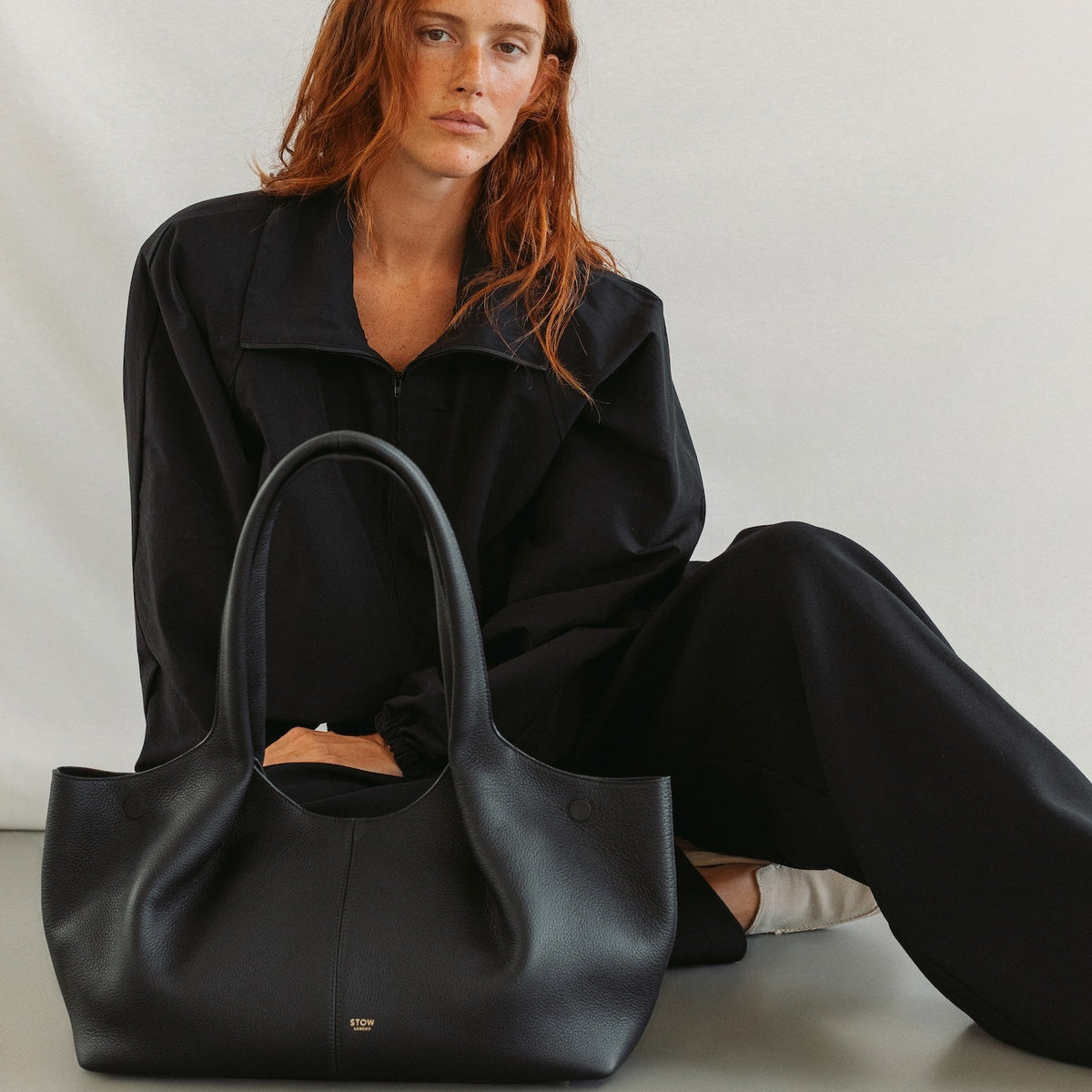 Model with STOW London's Hobo Tote in Black pebbled leather featuring a pleated front panel and gold-coated stainless steel hardware