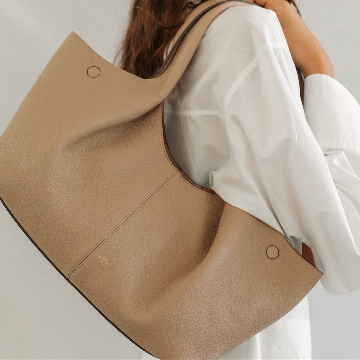 Model wearing STOW London's Hobo Tote in Camel pebbled leather featuring a pleated front panel and gold-coated stainless steel hardware