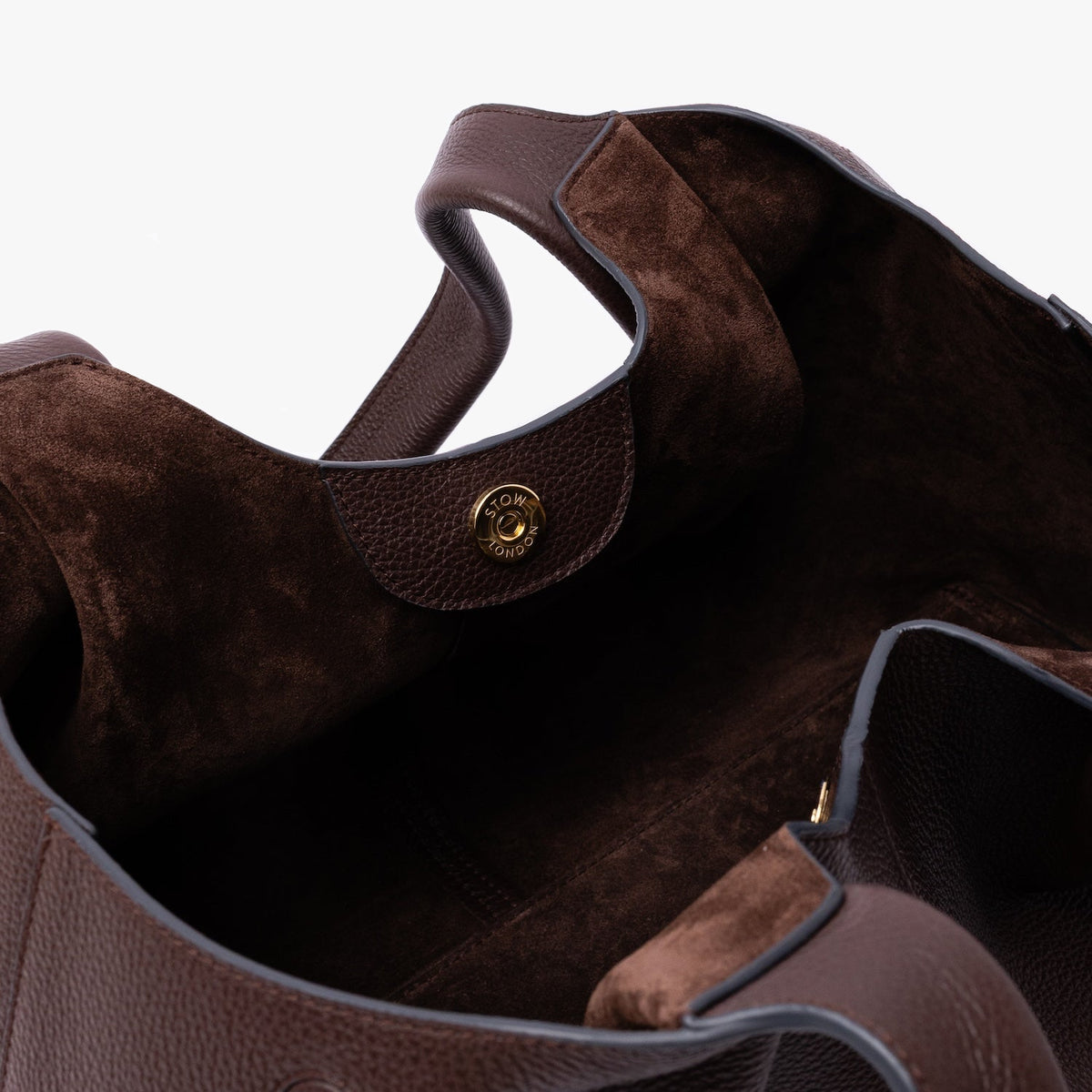 Close up of the Chocolate suede interior lining and gold magnetic closure on STOW London's Hobo Tote in Espresso pebbled leather on a light grey background