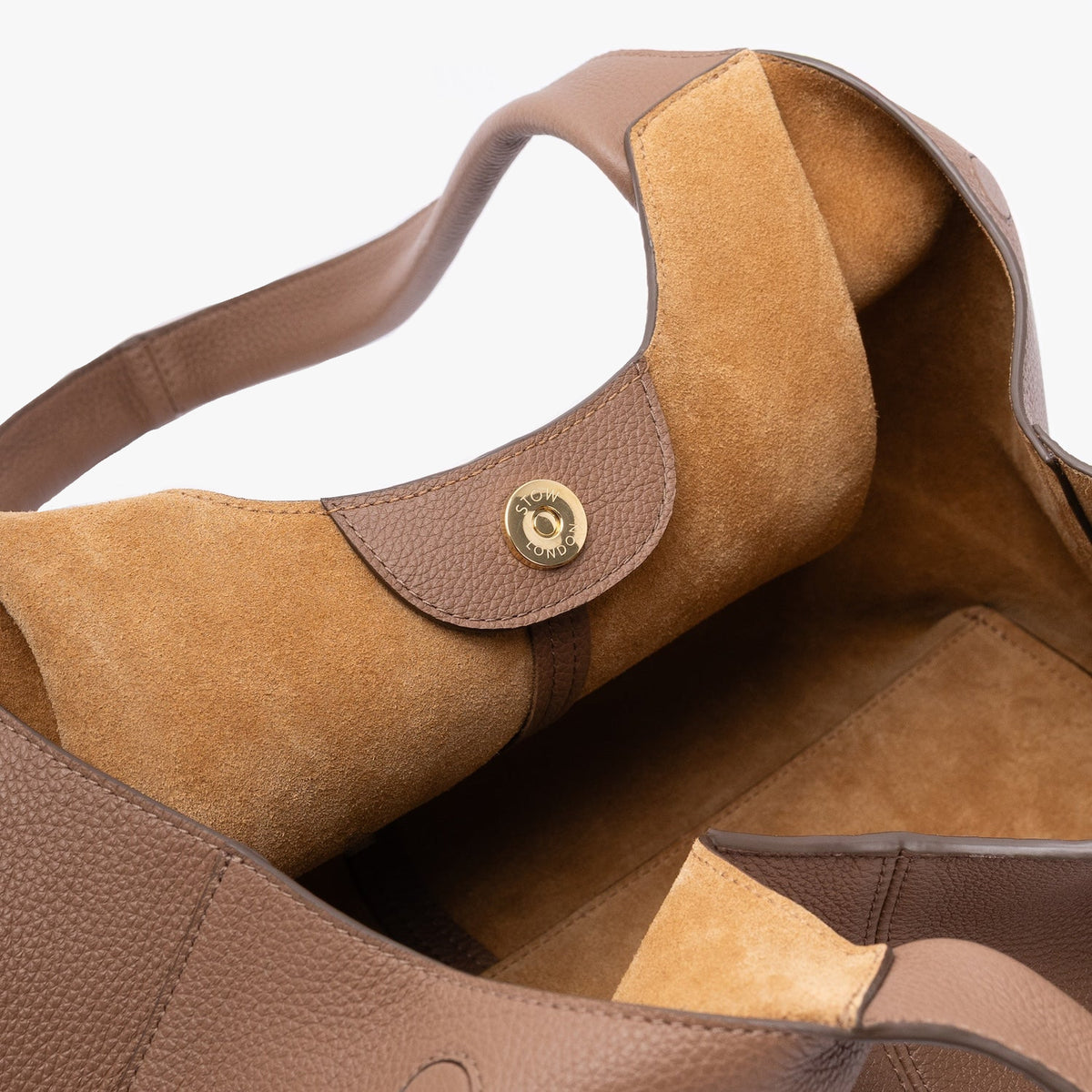 Close up of the suede interior lining and gold magnetic closure on STOW London's Hobo Tote in Mocha pebbled leather on a light grey background