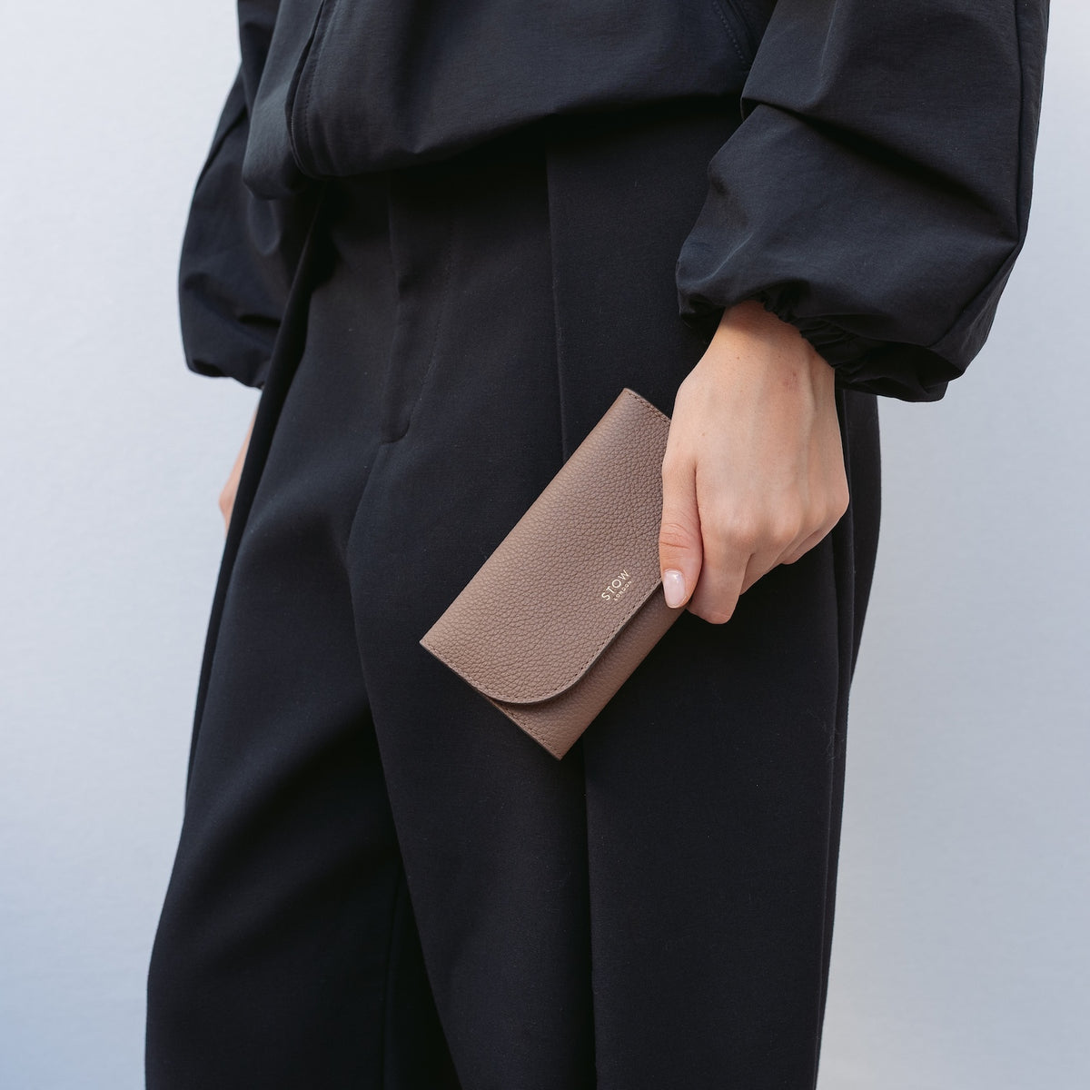 Model holding STOW London's Jewellery Roll in Mocha pebbled leather featuring a small gold embossed logo on the front