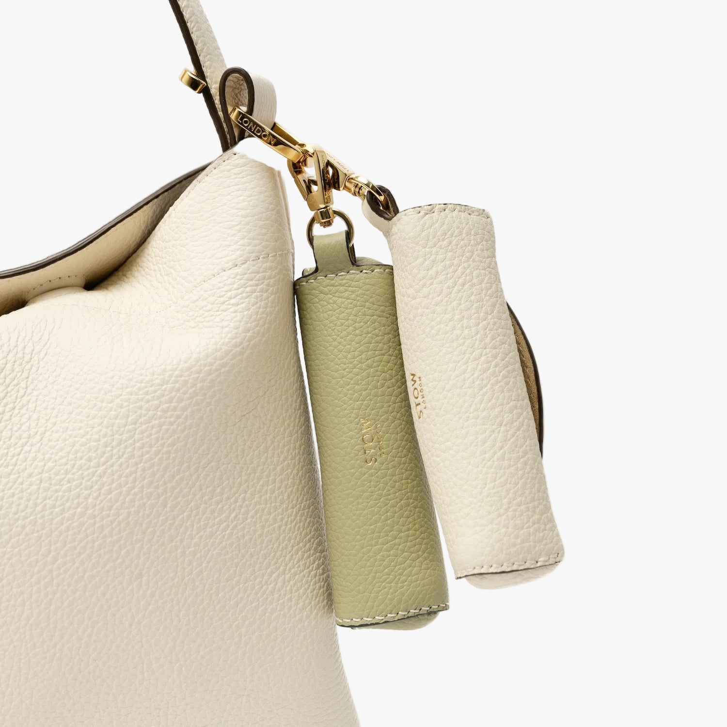 Close up of STOW London's Lipstick Case in Green pebbled leather attached to the Spring Moon Midi Curve in alongside the Spring Moon lipstick case on a light grey background featuring a gold-coated stainless steel clip