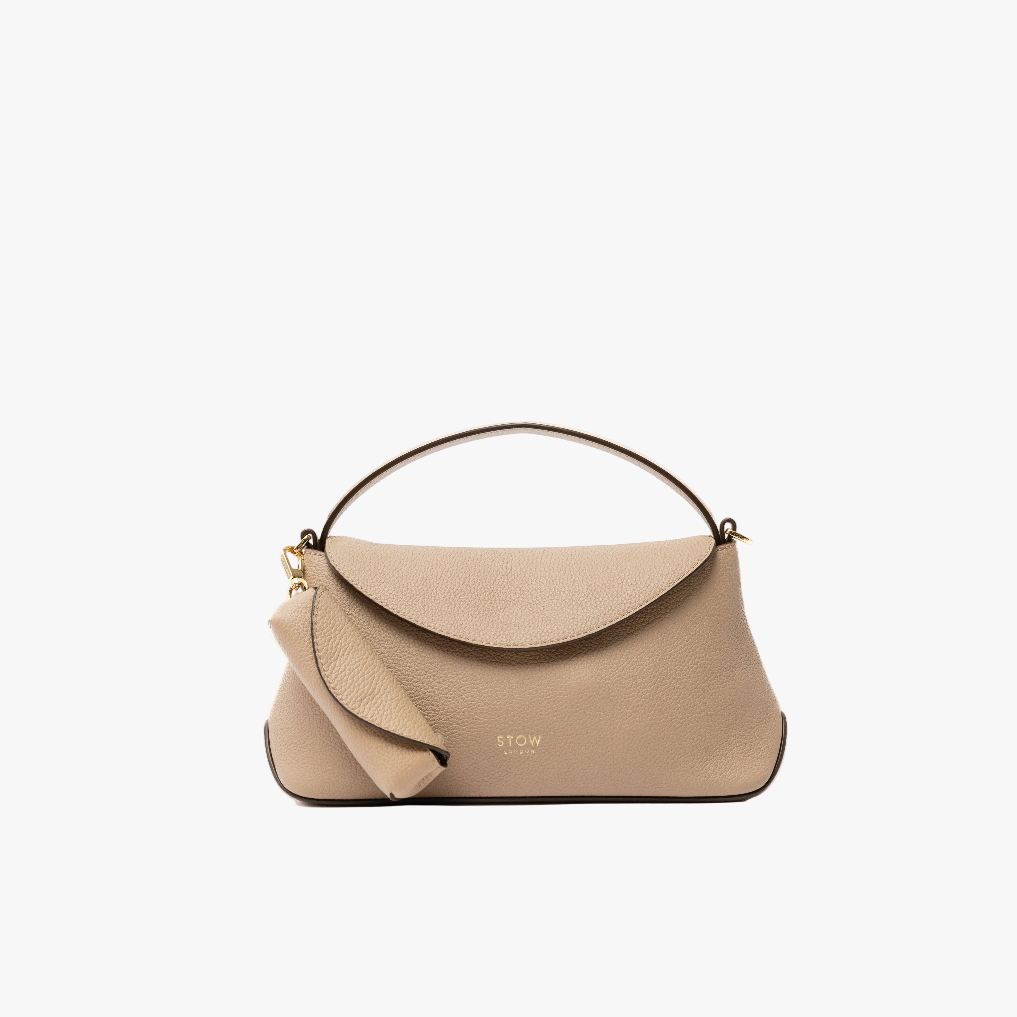 STOW London's Lipstick Case in Camel pebbled leather attached by a gold-coated stainless steel clip to the matching Mini East West Bag on a light grey background