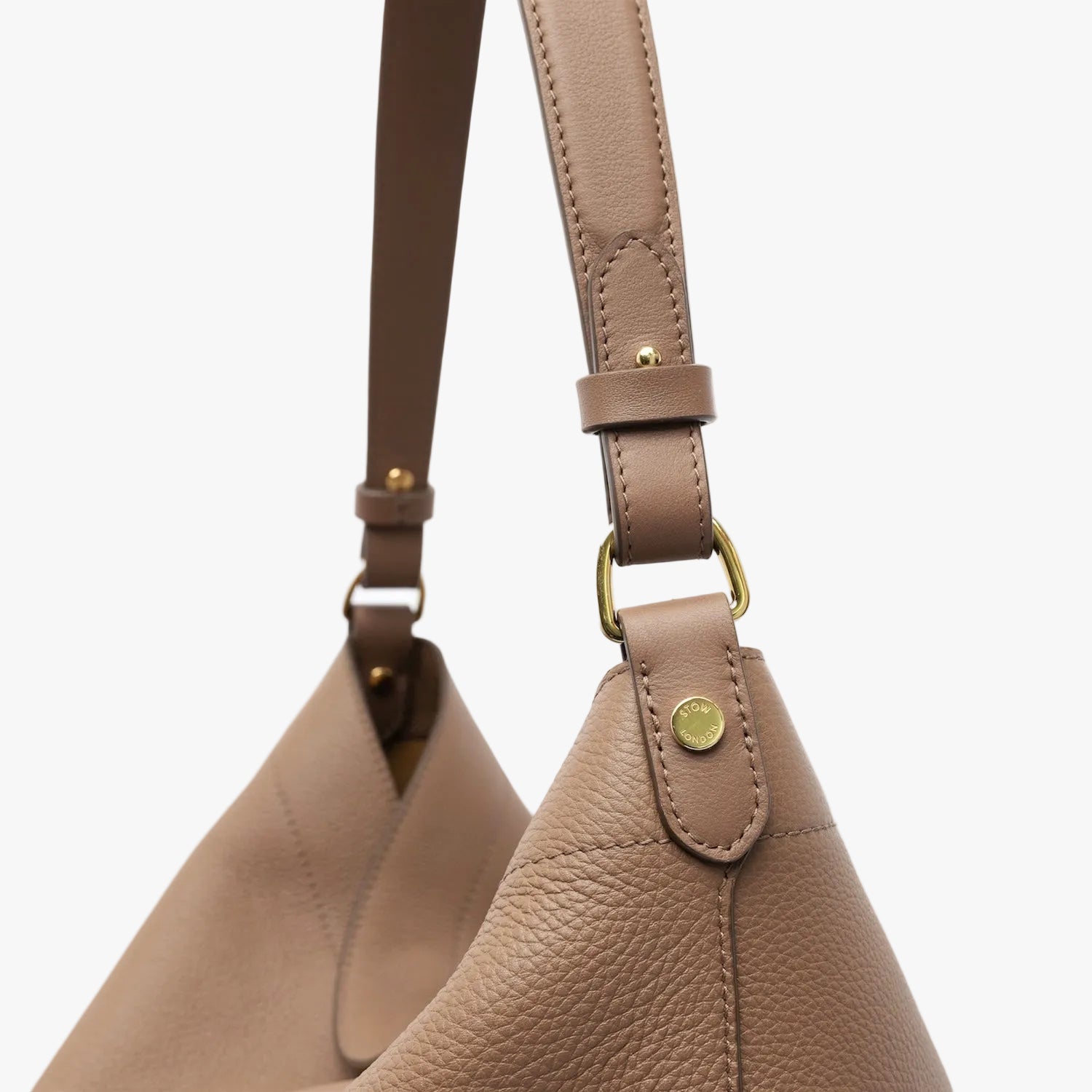 Close up of the the handle of STOW London's Maxi Curve bag in Mocha pebbled leather featuring gold-coated stainless steel hardware on a light grey background