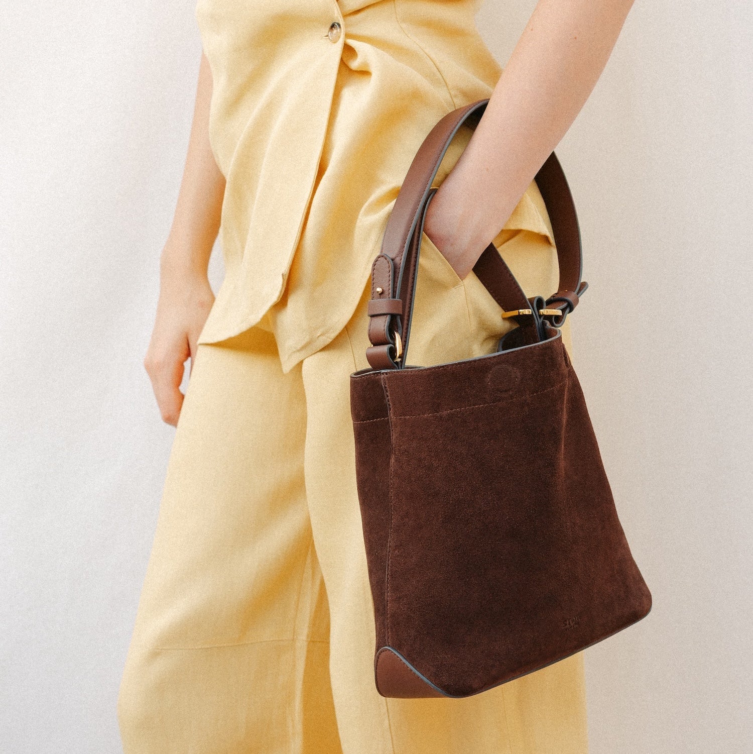 Model wearing STOW London's Midi Curve in Chocolate suede leather featuring the detachable shoulder strap with gold hardware