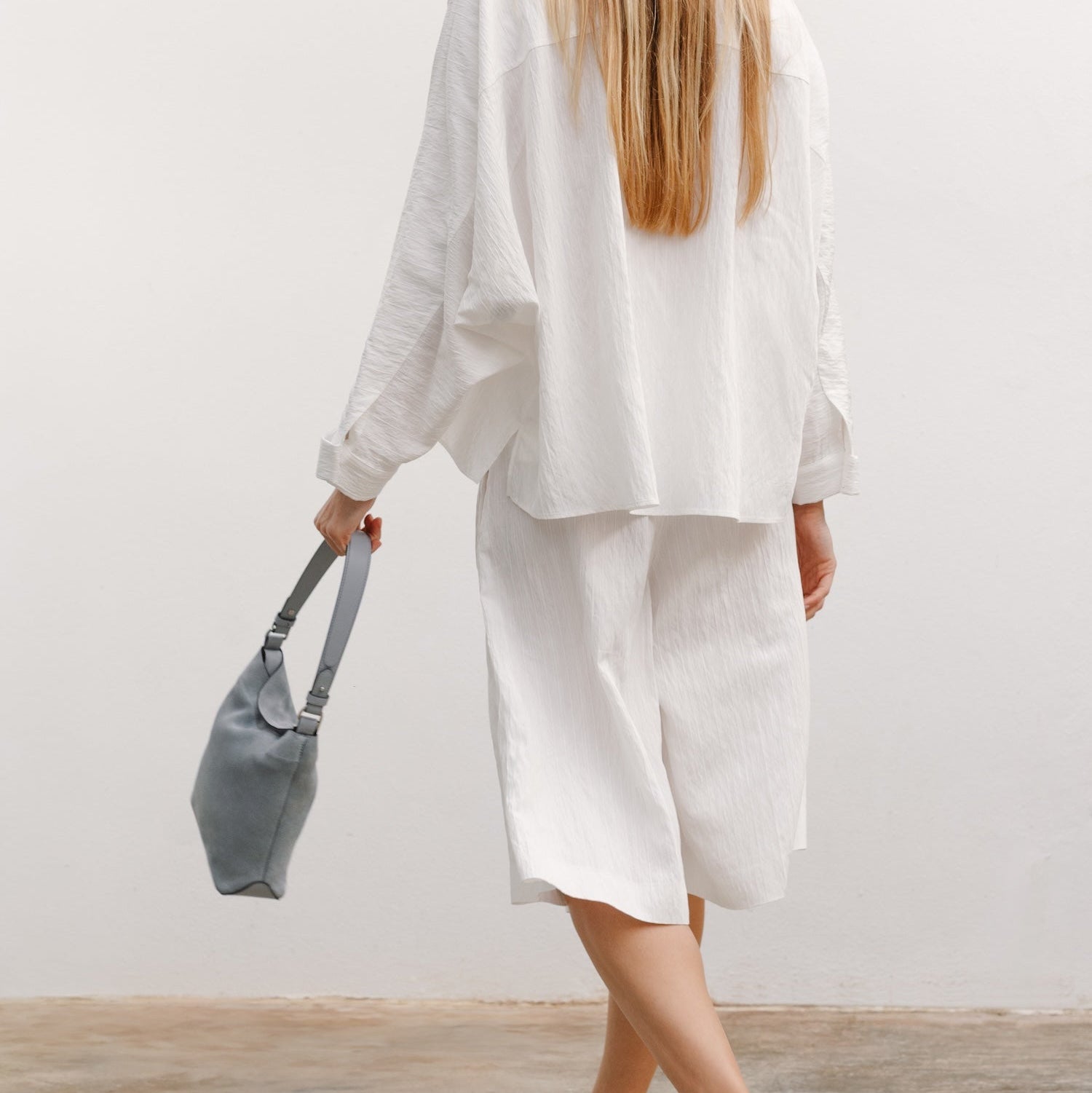 Model walking with STOW London's Midi Curve in Misty Blue suede featuring the detachable shoulder strap
