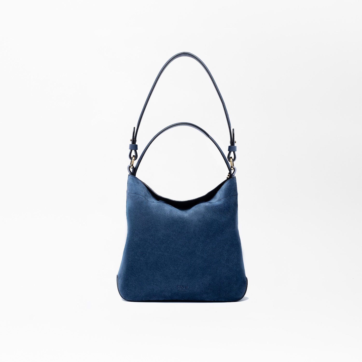 STOW London's Midi Curve in Navy suede leather on a light grey background featuring the detachable shoulder strap and top handle with gold hardware and details