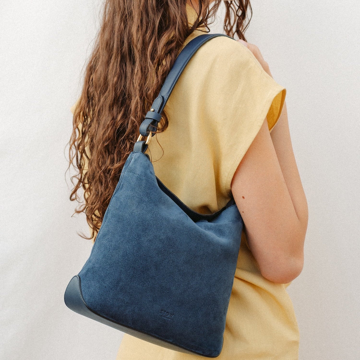 Model wearing STOW London's Midi Curve in Navy leather featuring the detachable shoulder strap with gold hardware