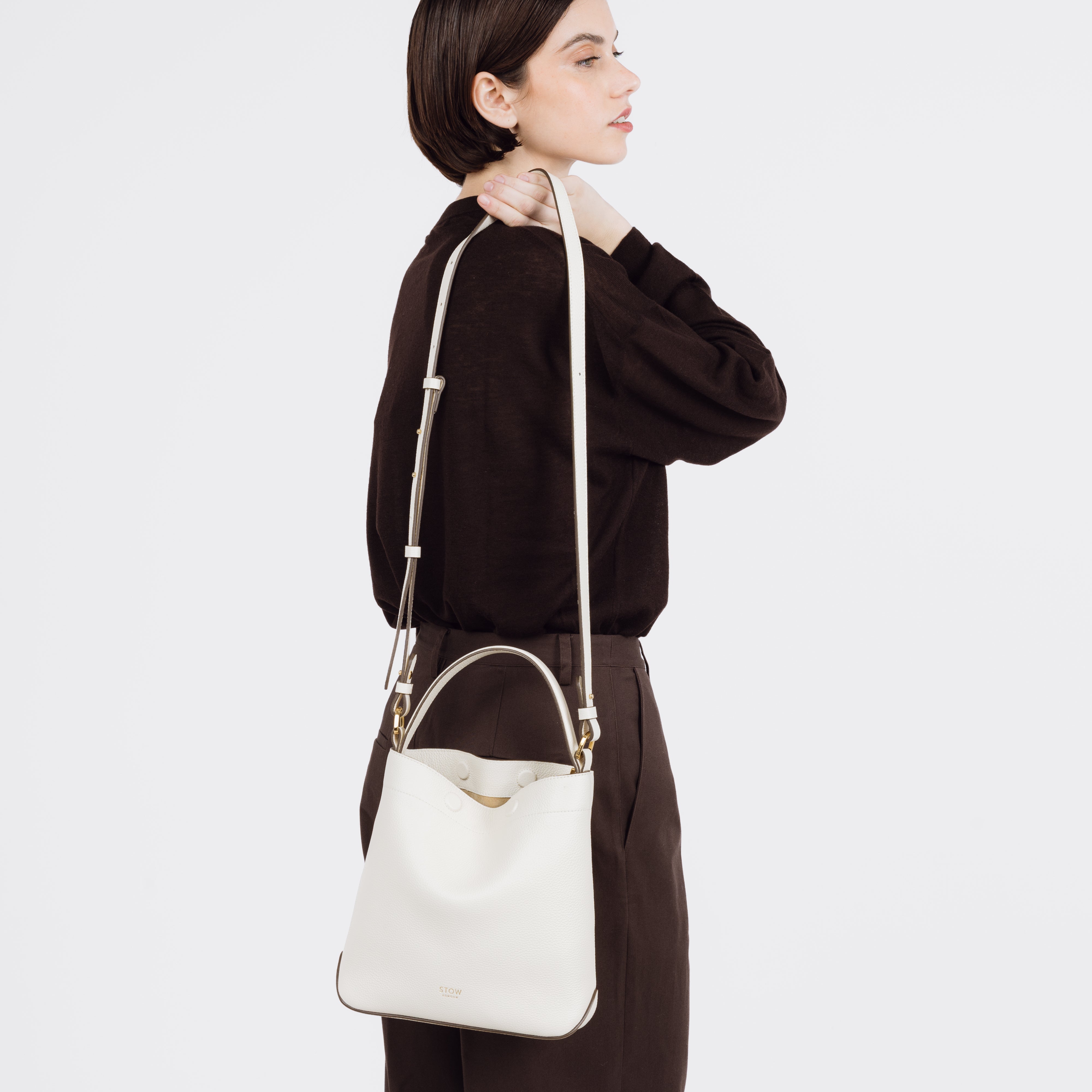 Model holding STOW London's Midi Curve bag in Spring Moon pebbled and smooth leather over her shoulder featuring gold-coated stainless steel hardware on a white background