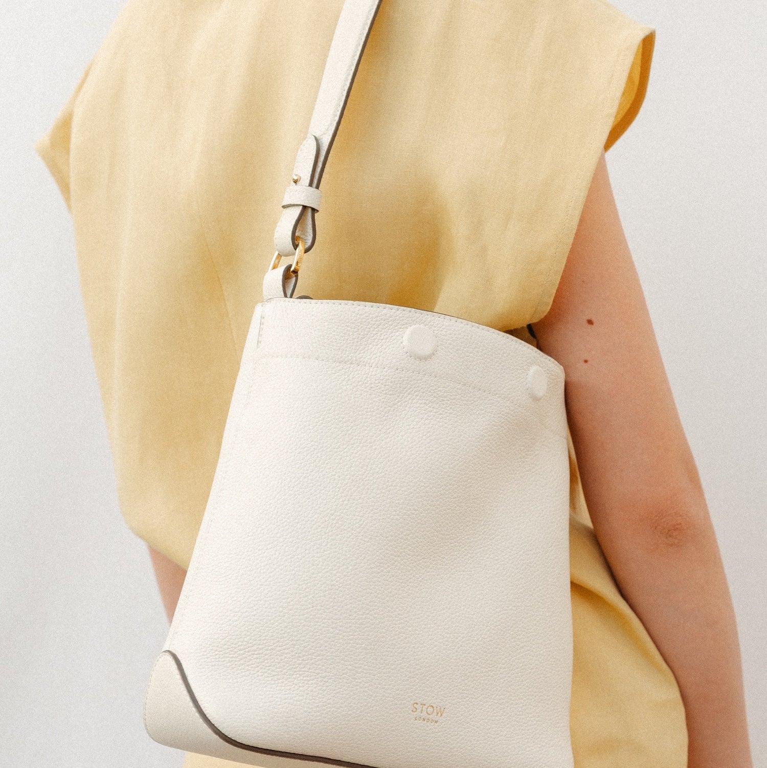Model wearing STOW London's Midi Curve in Spring Moon leather featuring the detachable shoulder strap with gold hardware and details
