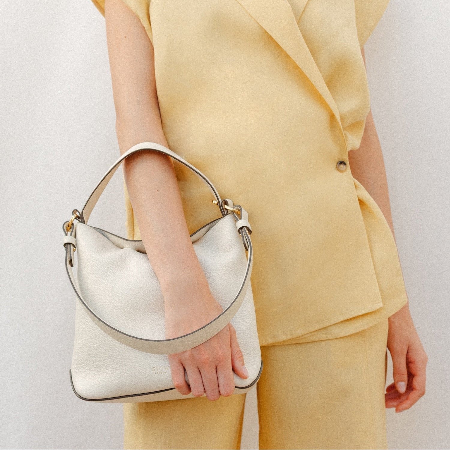 Model holding STOW London's Midi Curve in Spring Moon leather featuring the detachable shoulder strap with gold hardware and details