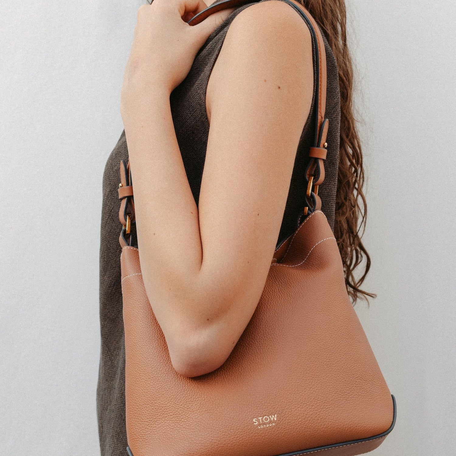 Model wearing STOW London's Curve in Earth Tan leather featuring the detachable shoulder strap with gold hardware and details