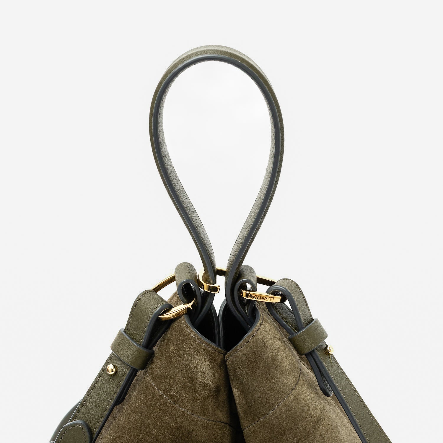 Close up of the handles on STOW London's Midi Curve in Dark Green suede leather featuring gold-coated stainless steel hardware, clip and detachable strap on a light grey background