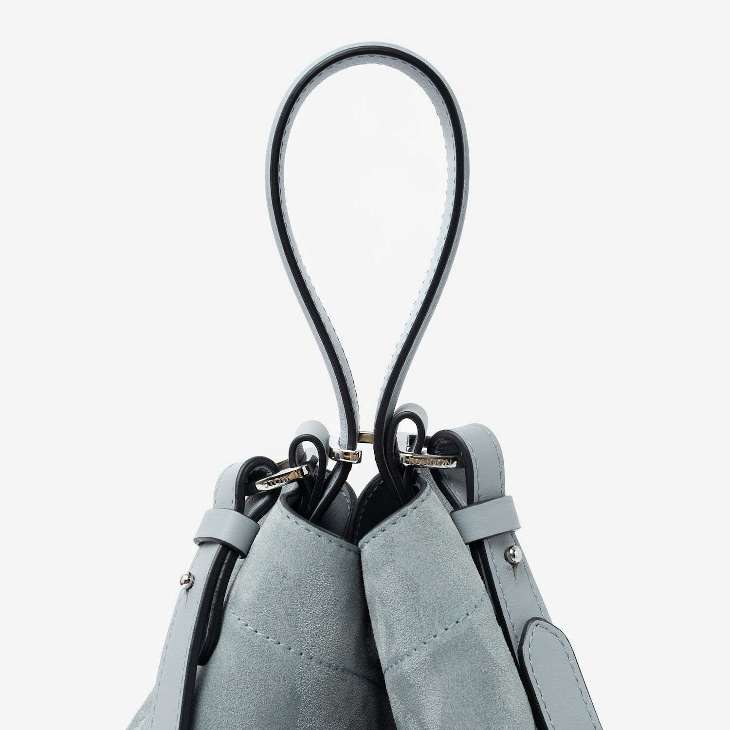 Close up of the handle on STOW London's Midi Curve in Misty Blue suede leather featuring silver stainless steel hardware, clip and detachable crossbody strap on a light grey background