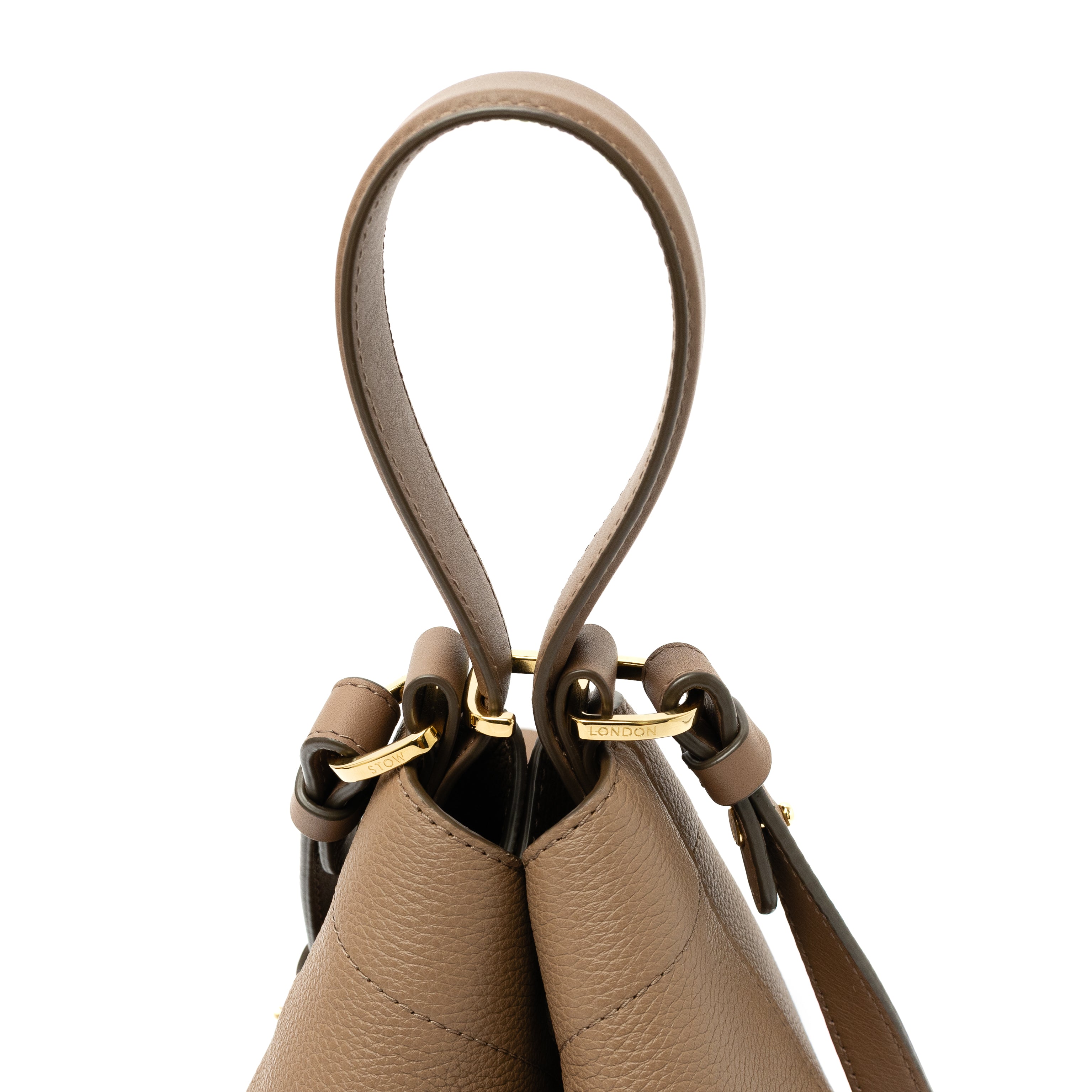 Close up view of top handle, clip and detachable strap on STOW London's Midi Curve bag in Mocha pebbled and smooth leather featuring gold-coated stainless steel hardware on a white background
