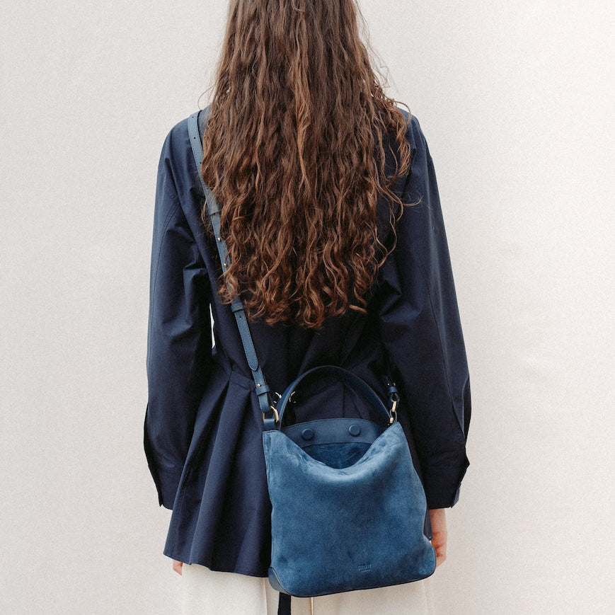 Model wearing STOW London's Midi Curve in Navy suede leather crossbody featuring gold-coated stainless steel hardware