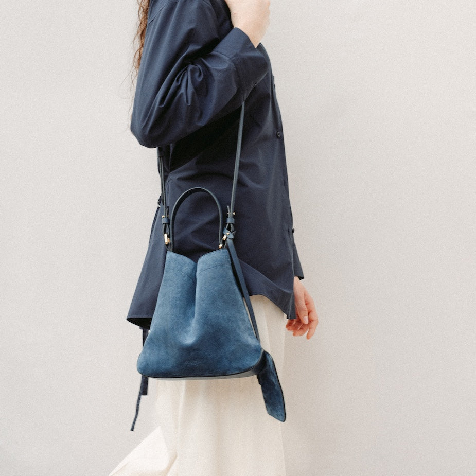 Model wearing STOW London's Midi Curve in Navy suede leather on her shoulder styled in a triangular form featuring gold-coated stainless steel hardware