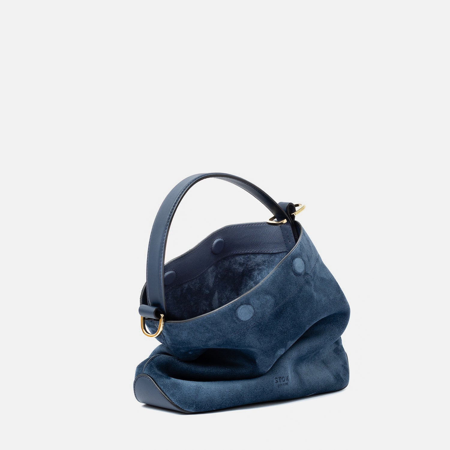Off-axis view of STOW London's Midi Curve in Navy suede leather with magnets open showing suede interior featuring gold-coated stainless steel hardware on a light grey background