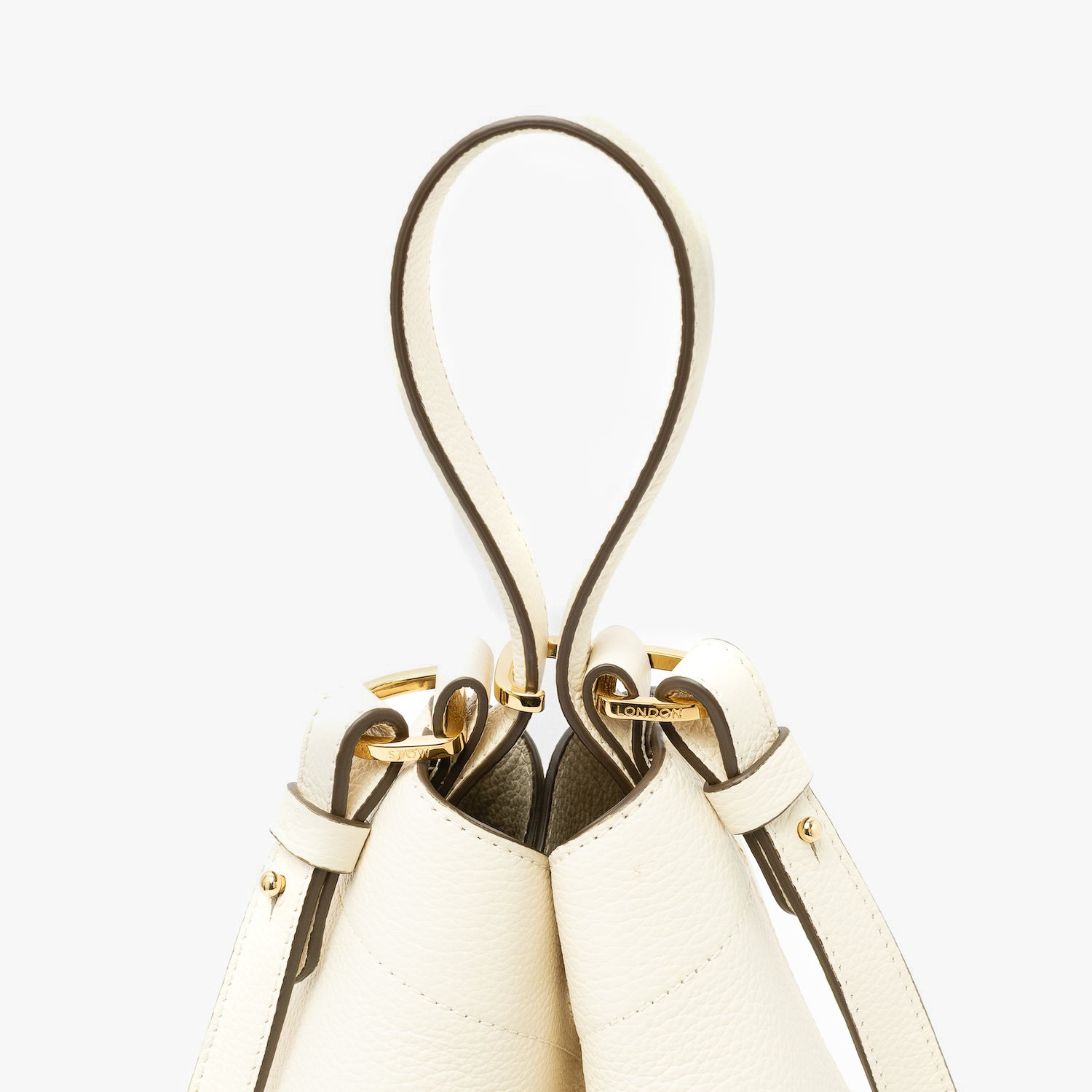 Close up of the handles on STOW London's Midi Curve in Spring Moon pebbled leather featuring gold-coated stainless steel hardware, clip and detachable strap on a light grey background