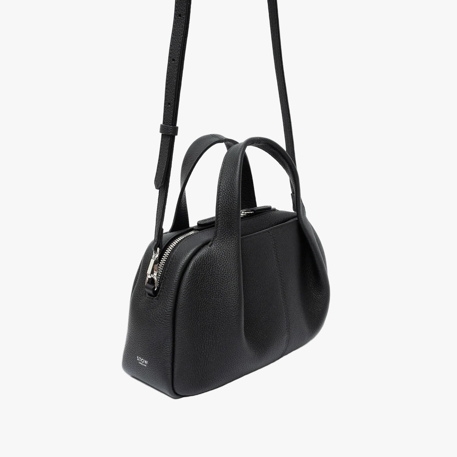 Off-axis view of STOW London's Mini Bowling bag in Black pebbled leather featuring a pleated front panel, detachable crossbody strap and silver stainless steel hardware on a light grey background