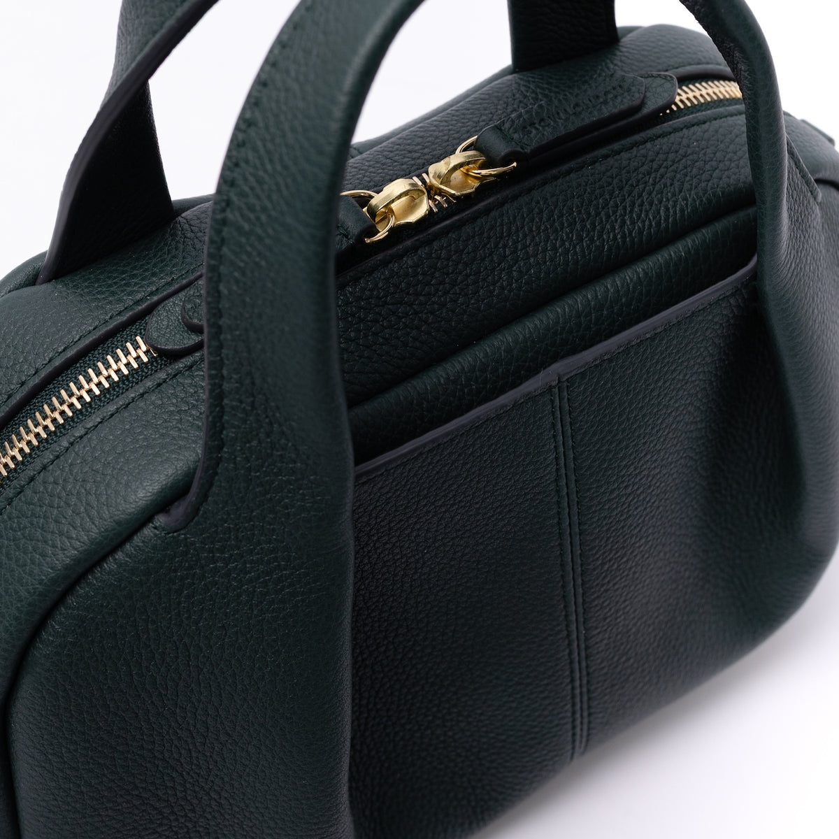 Close up of the gold zipper, pleated panel and exterior slip pocket on STOW London's Mini Bowling in New Forest pebbled leather on a light grey background