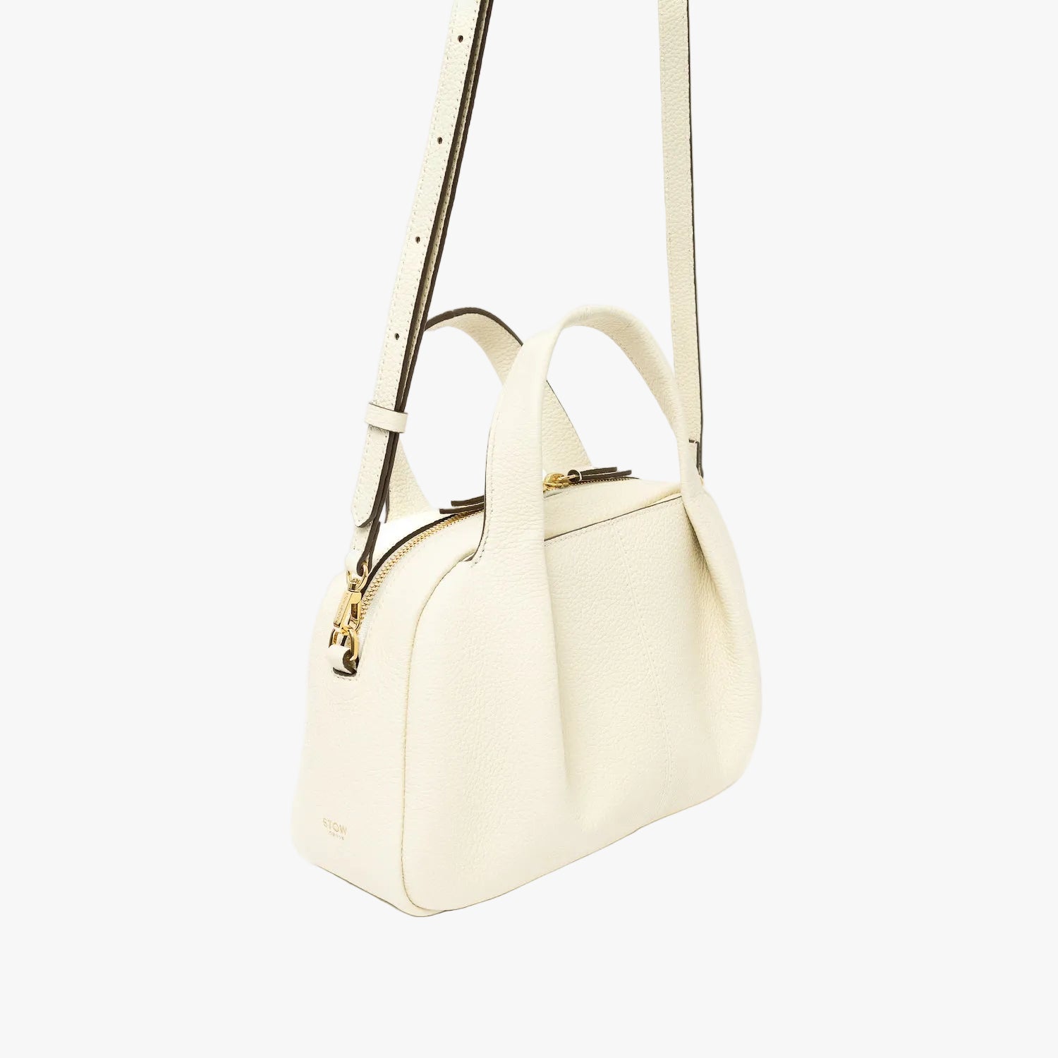 Off-axis view of STOW London's Mini Bowling bag in Spring Moon pebbled leather featuring a pleated front panel, detachable crossbody strap and gold-coated stainless steel hardware on a light grey background