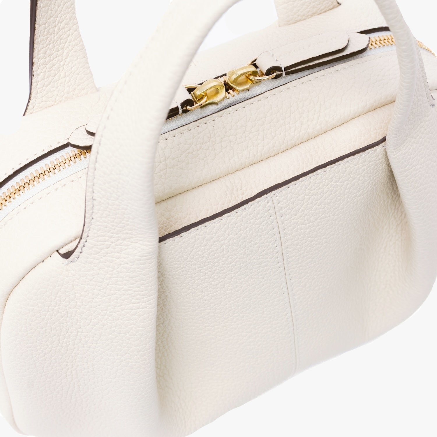Close up of STOW London's Mini Bowling bag in Spring Moon pebbled leather featuring a pleated front panel and gold-coated stainless steel hardware and zip on a light grey background
