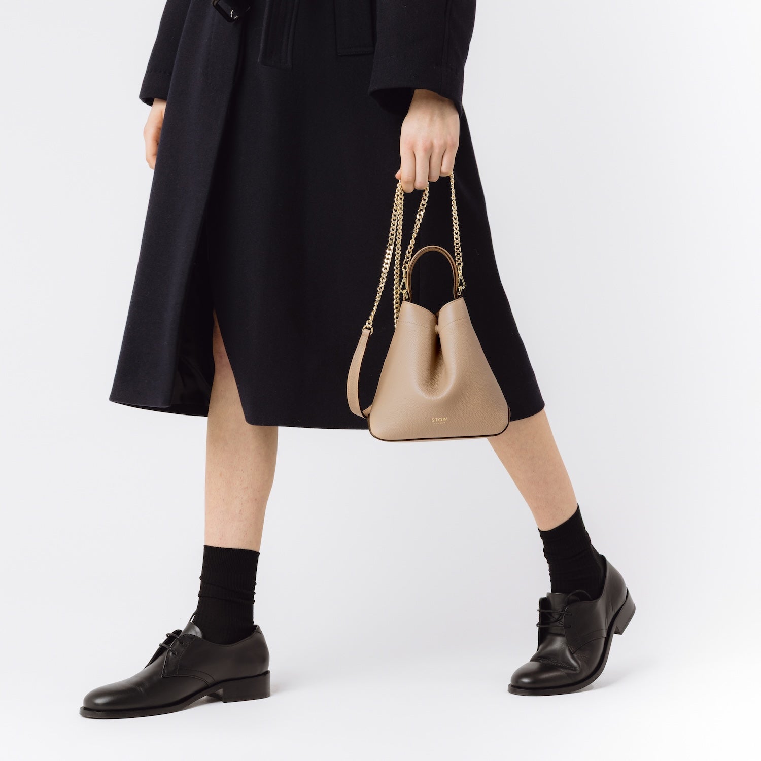Model with STOW London's Mini Curve in Camel leather featuring the gold-plated chain on a white background