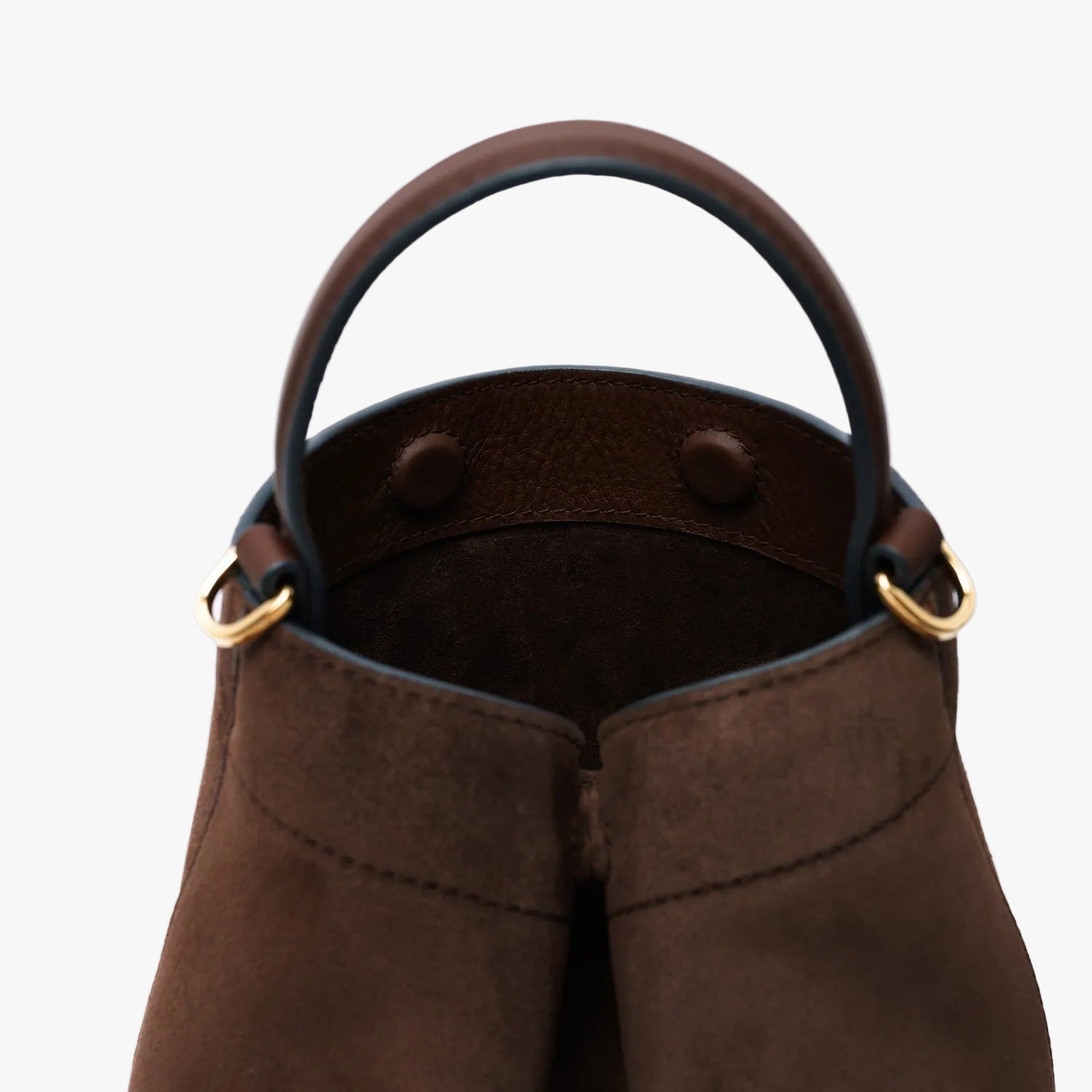 Close up of the top handle on STOW London's Mini Curve in Chocolate suede leather on a light grey background featuring gold-coated stainless steel hardware