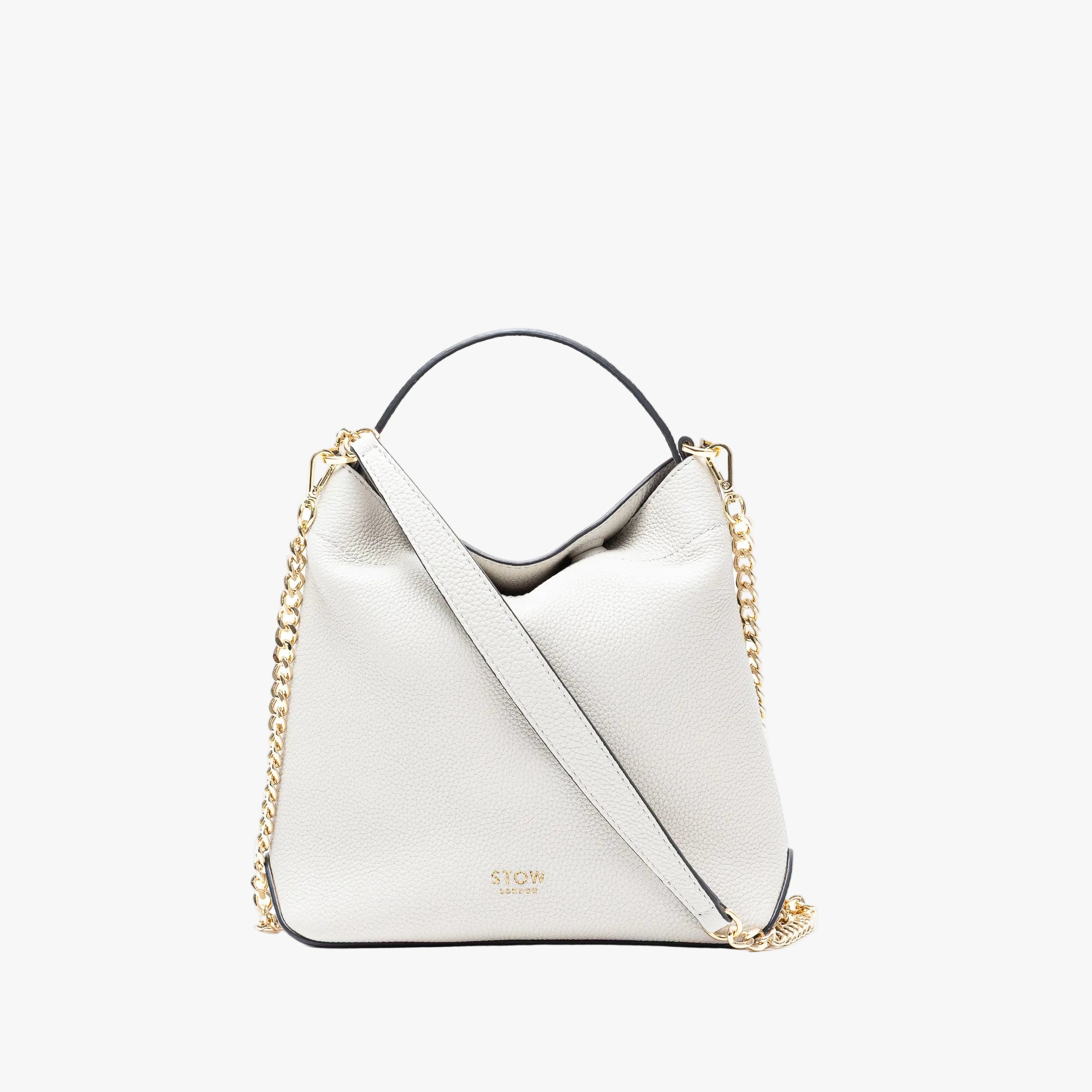 Stow London's Mini Curve in Cloud Grey pebbled leather and detachable gold chain crossbody strap on a light grey background