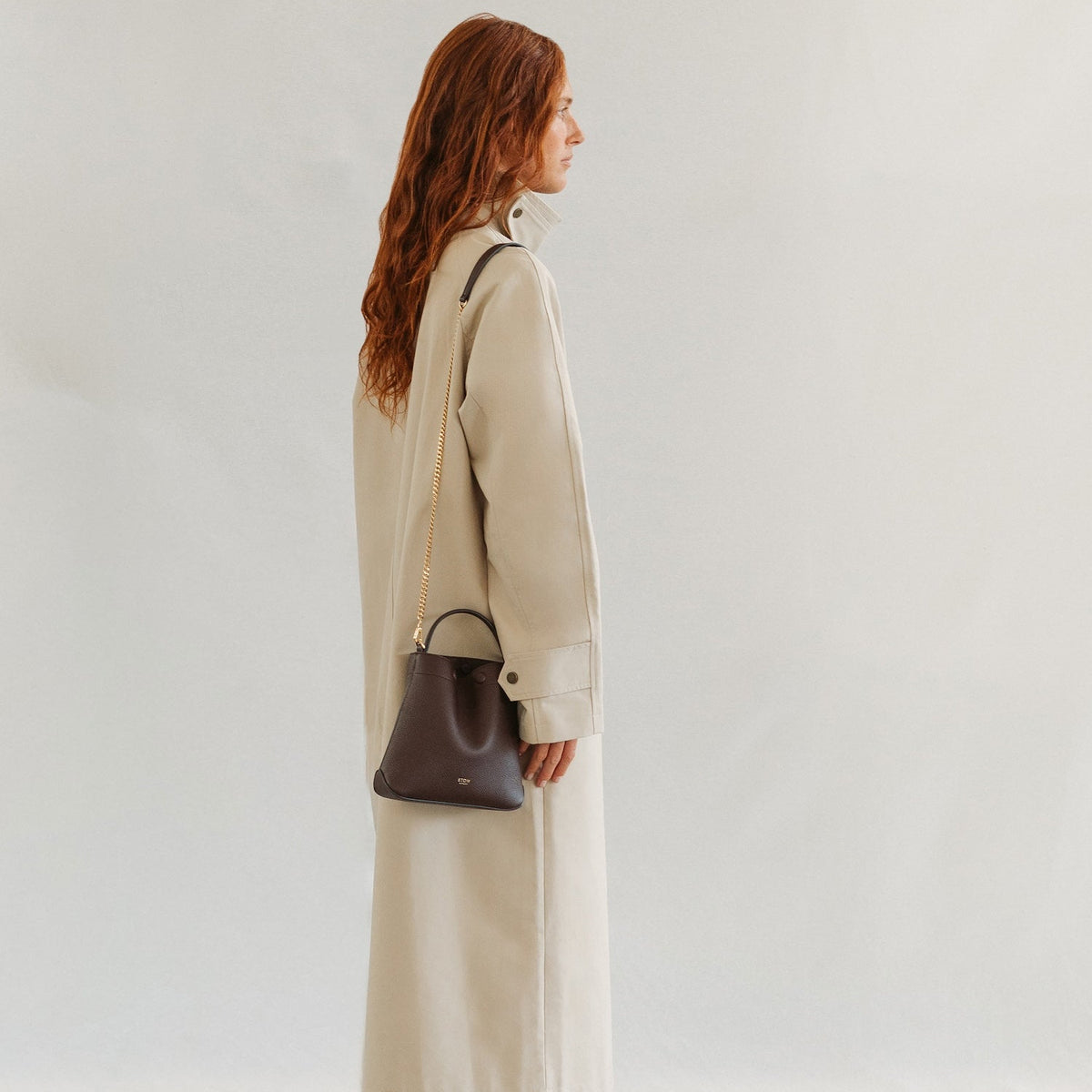 Model wearing STOW London's Mini Curve in Espresso pebbled leather on her shoulder featuring the detachable gold chain strap