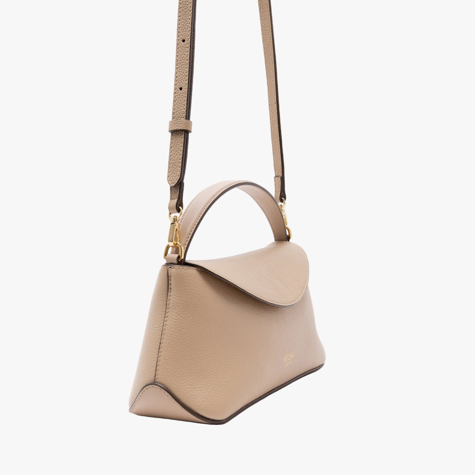 Off-axis view of STOW London's Mini East West in Camel pebbled leather and detachable crossbody strap featuring gold-coated stainless steel hardware on a light grey background