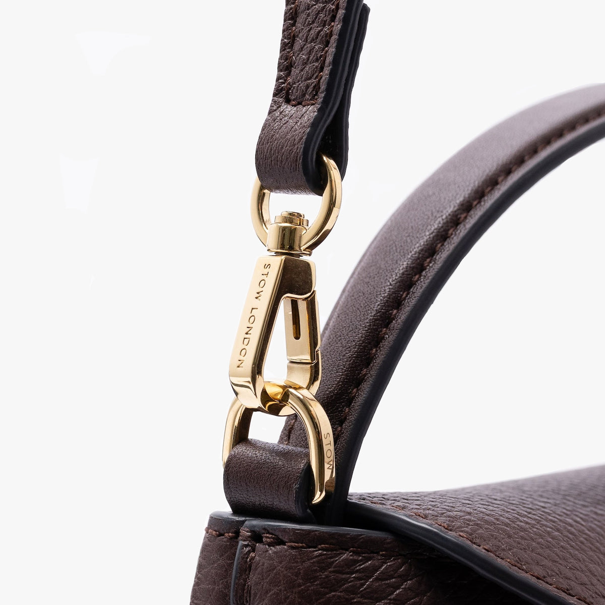 Close up of the gold-coated stainless steel hardware on STOW London's Mini East West in Espresso pebbled leather on a light grey background