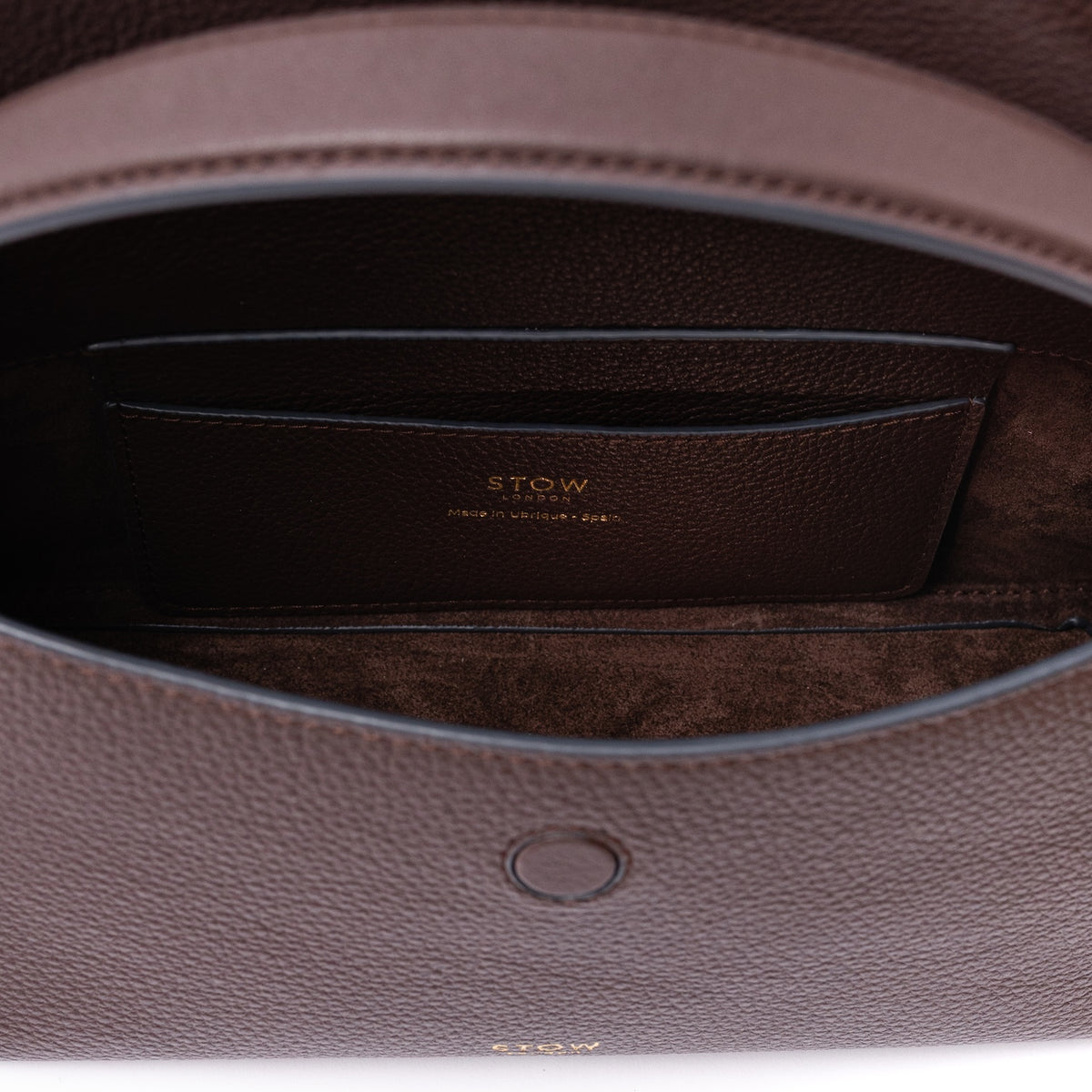 Close up of the interior of STOW London's Mini East West in Espresso pebbled leather on a light grey background featuring a chocolate suede lining and leather slip pocket
